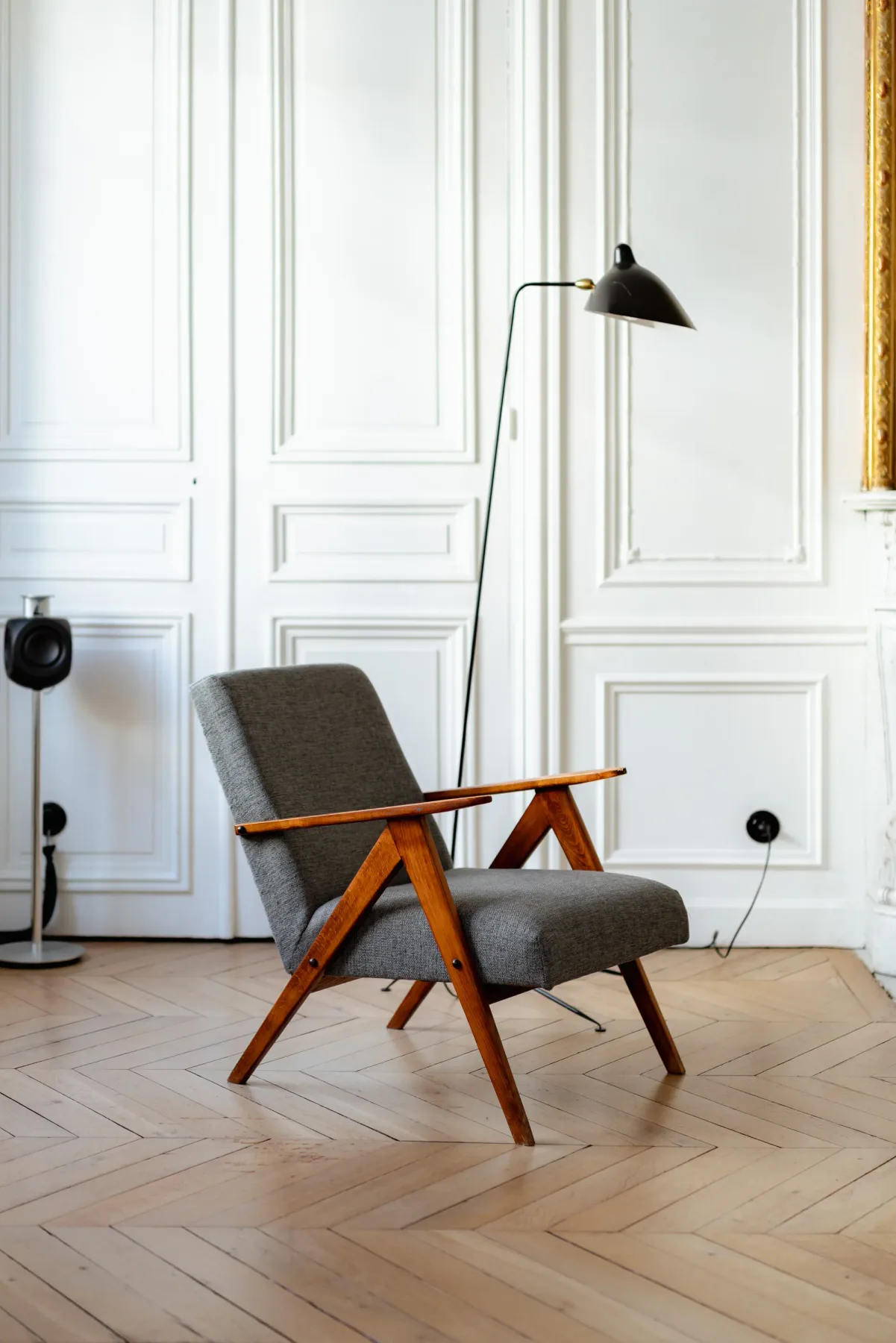 A gray lounge chair and floor lamp sit in a bright room with paneled walls.