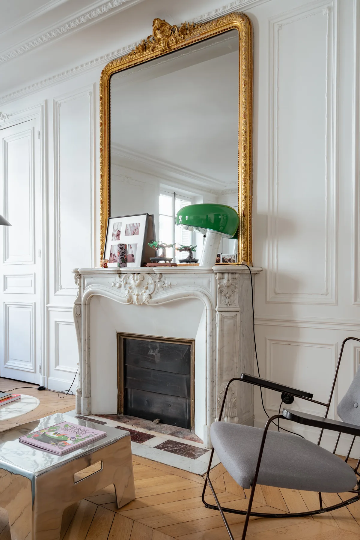 A bright sitting room features a white fireplace, ornate mirror, and seating.
