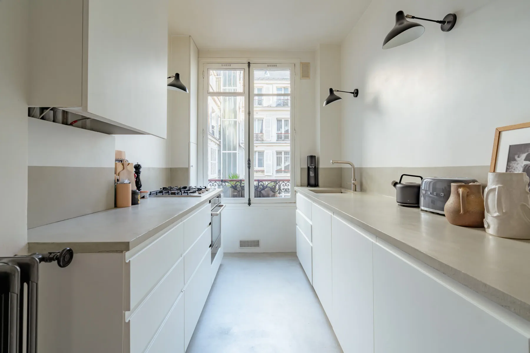 A bright kitchen with white cabinetry, counters, and tall windows at the far end.