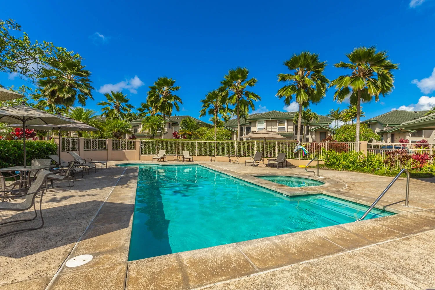 An outdoor swimming pool with a raised spa, lounge seating, and palm trees.