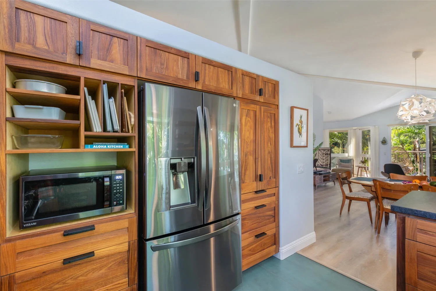 A kitchen with wooden cabinetry and a stainless steel refrigerator opens onto a dining area.