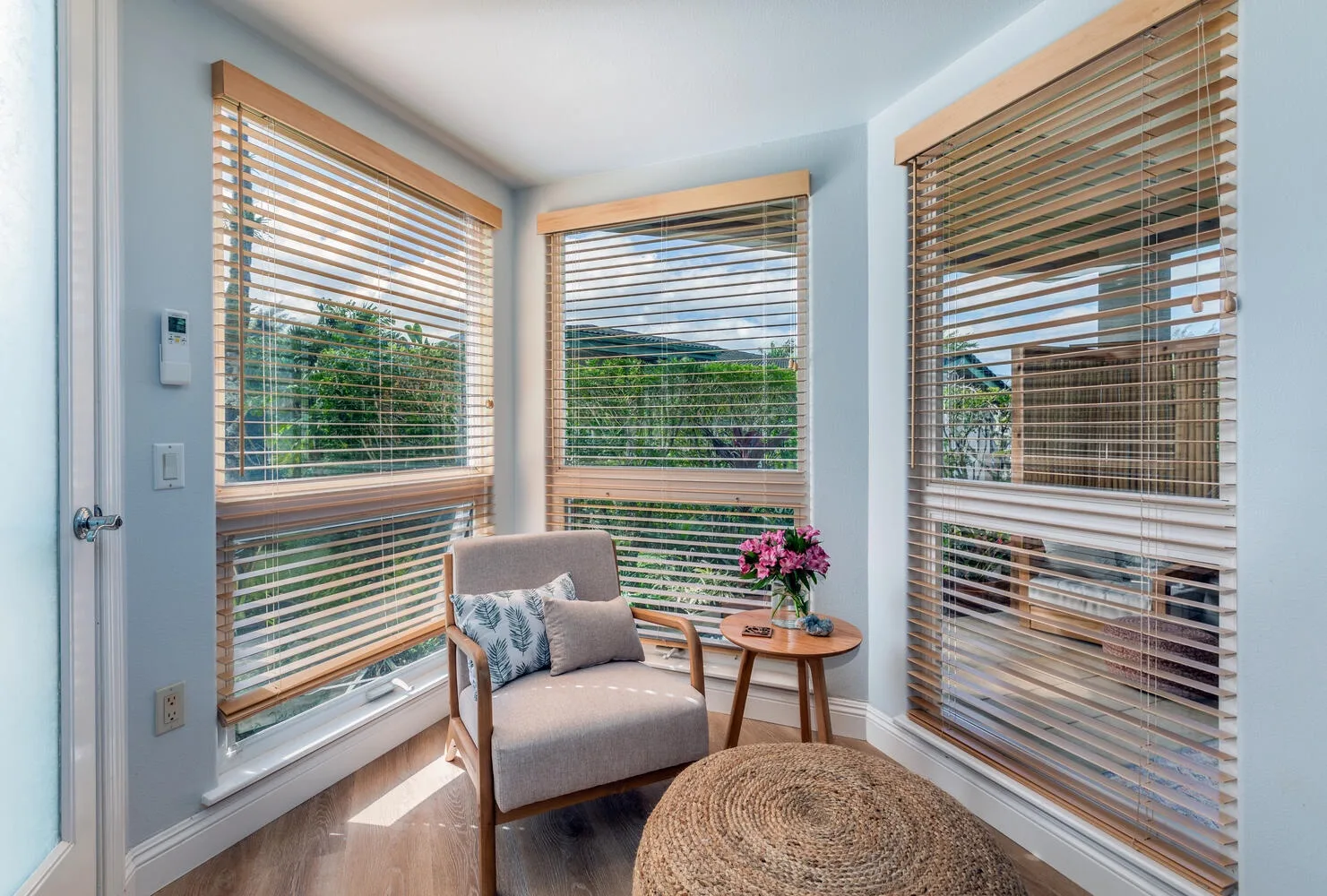 A bright sitting area with a cushioned chair beside windows with wooden blinds.