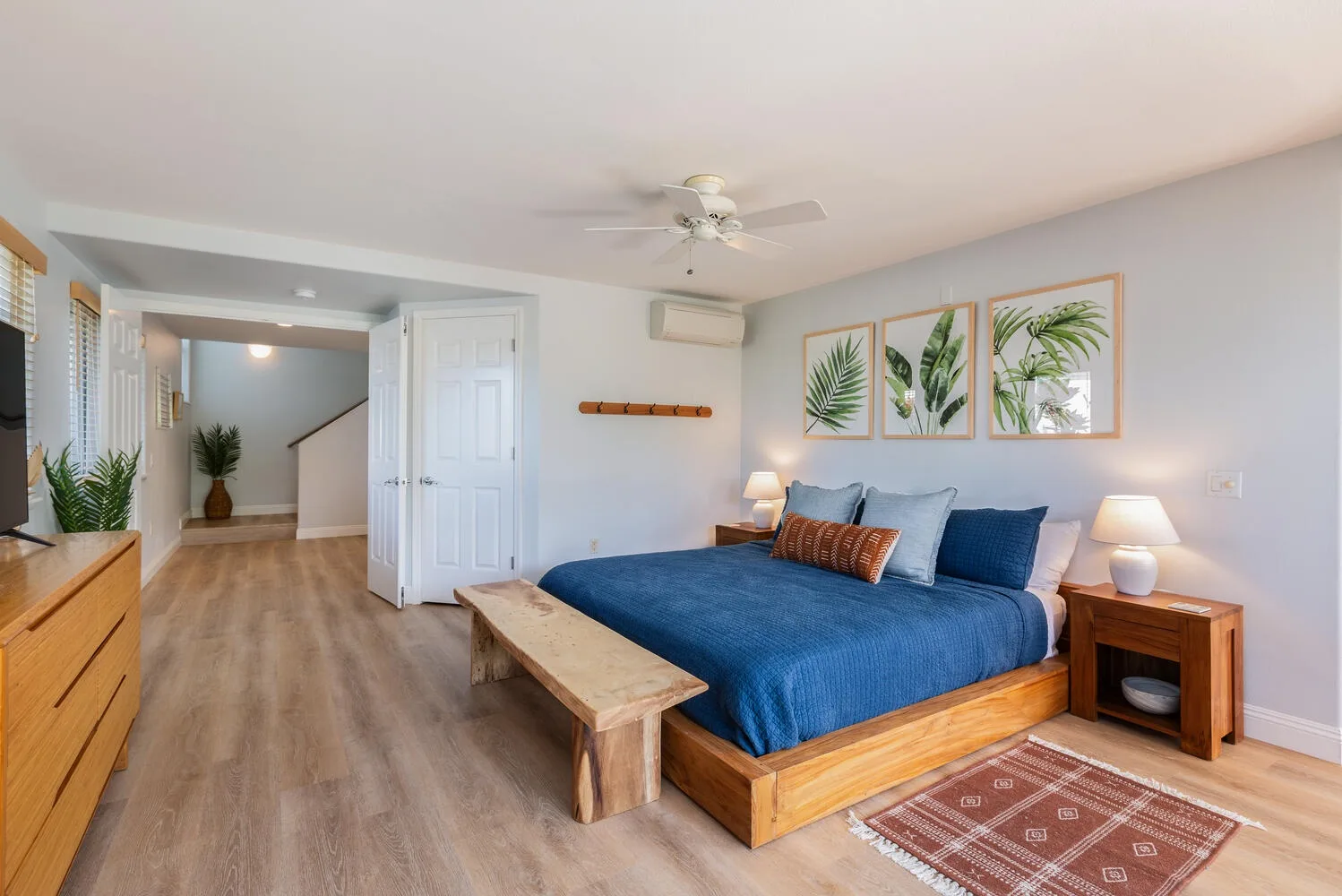 A bedroom with a blue bed, bedside tables, and framed botanical prints.