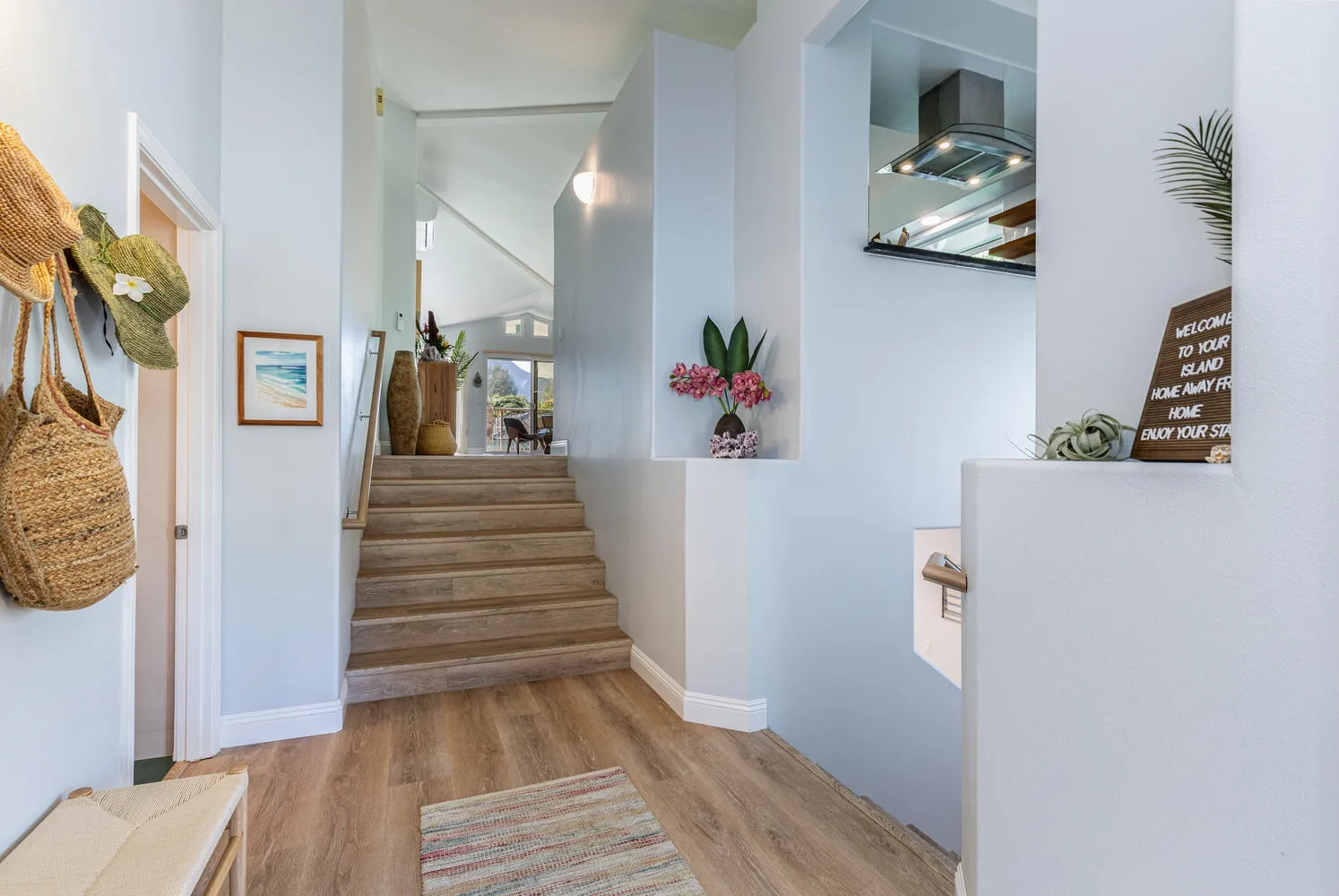 A bright interior entryway opens toward a raised area, with wood steps and a woven floor rug.