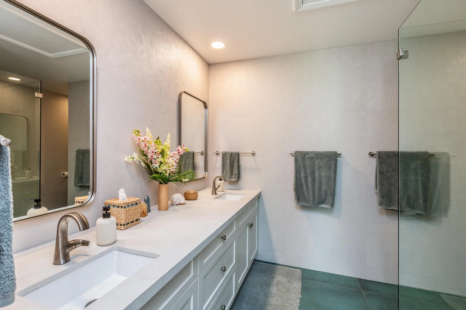 A bathroom vanity with a sink and towels beside a glass shower.