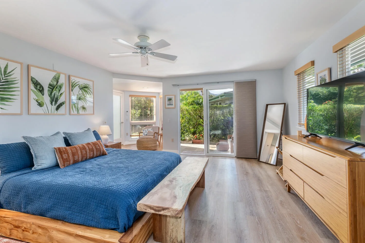 A bright bedroom with a blue bed, framed botanical prints, and sliding glass doors.