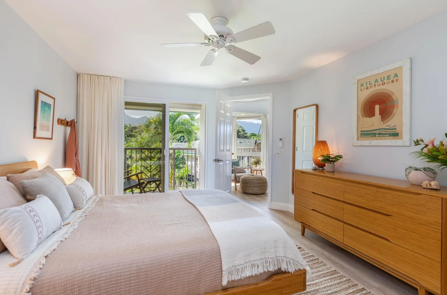 A bright bedroom with a bed, a wooden dresser, and an open balcony doorway.
