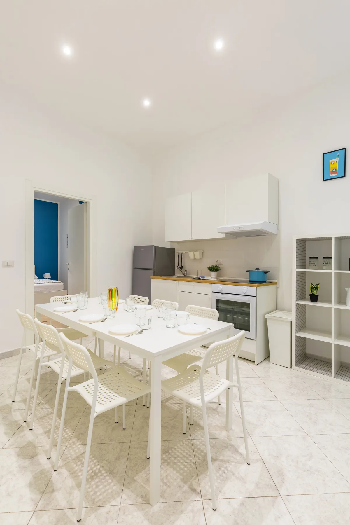 A bright dining area with a long table and an open kitchen behind it.