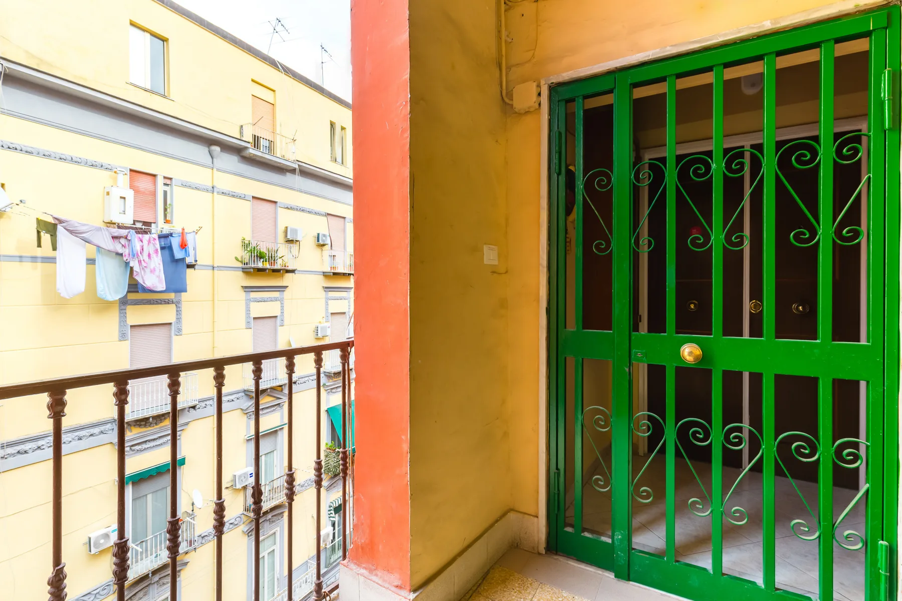 A green metal security gate opens onto a small balcony facing neighboring buildings.