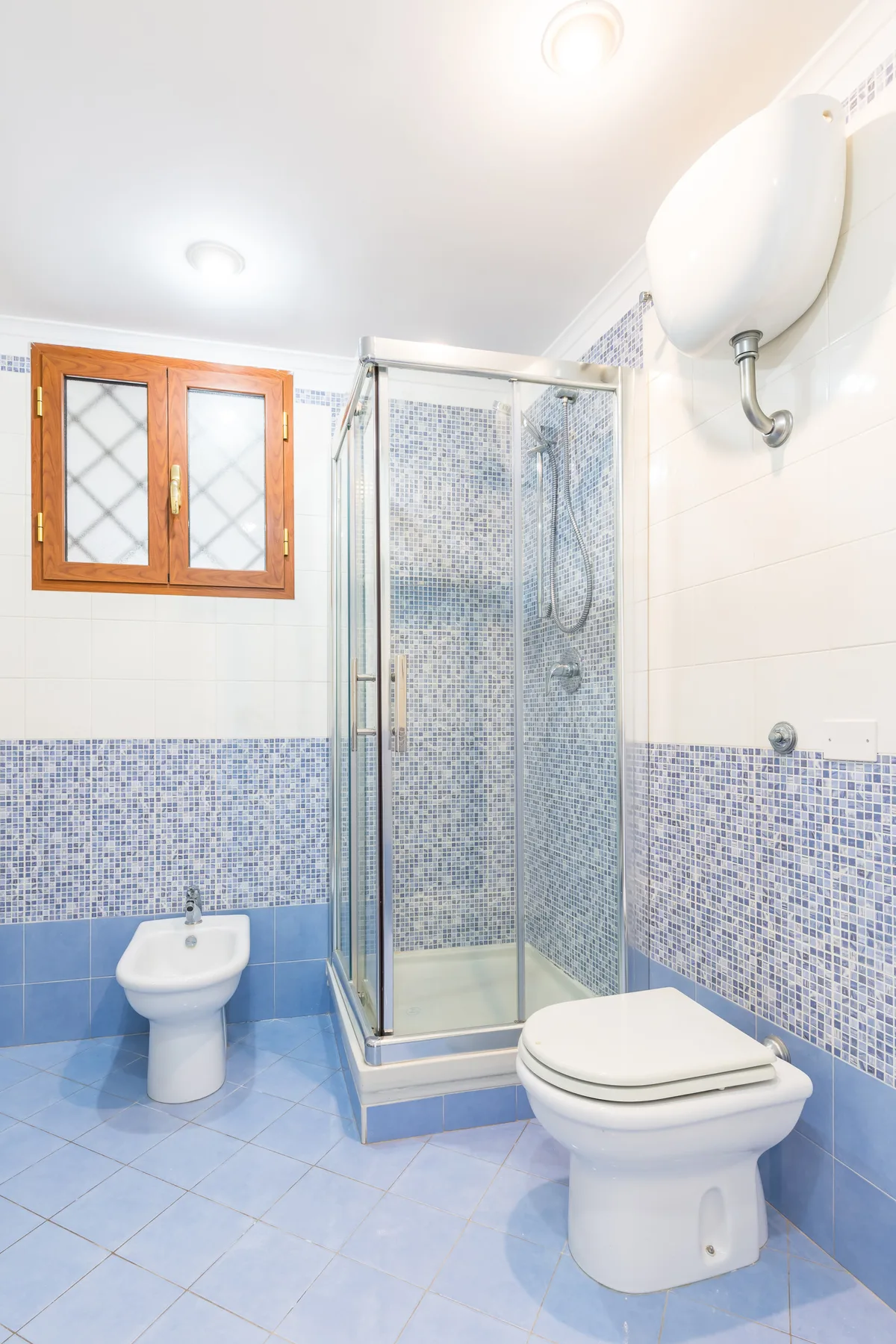 A tiled bathroom with a glass shower, toilet, and small window.
