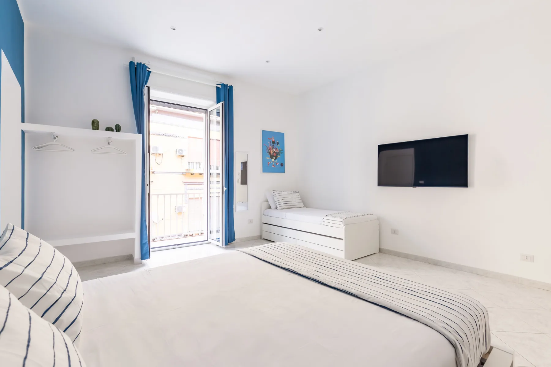 A bright bedroom with a bed, a wall-mounted television, and blue curtains by the window.