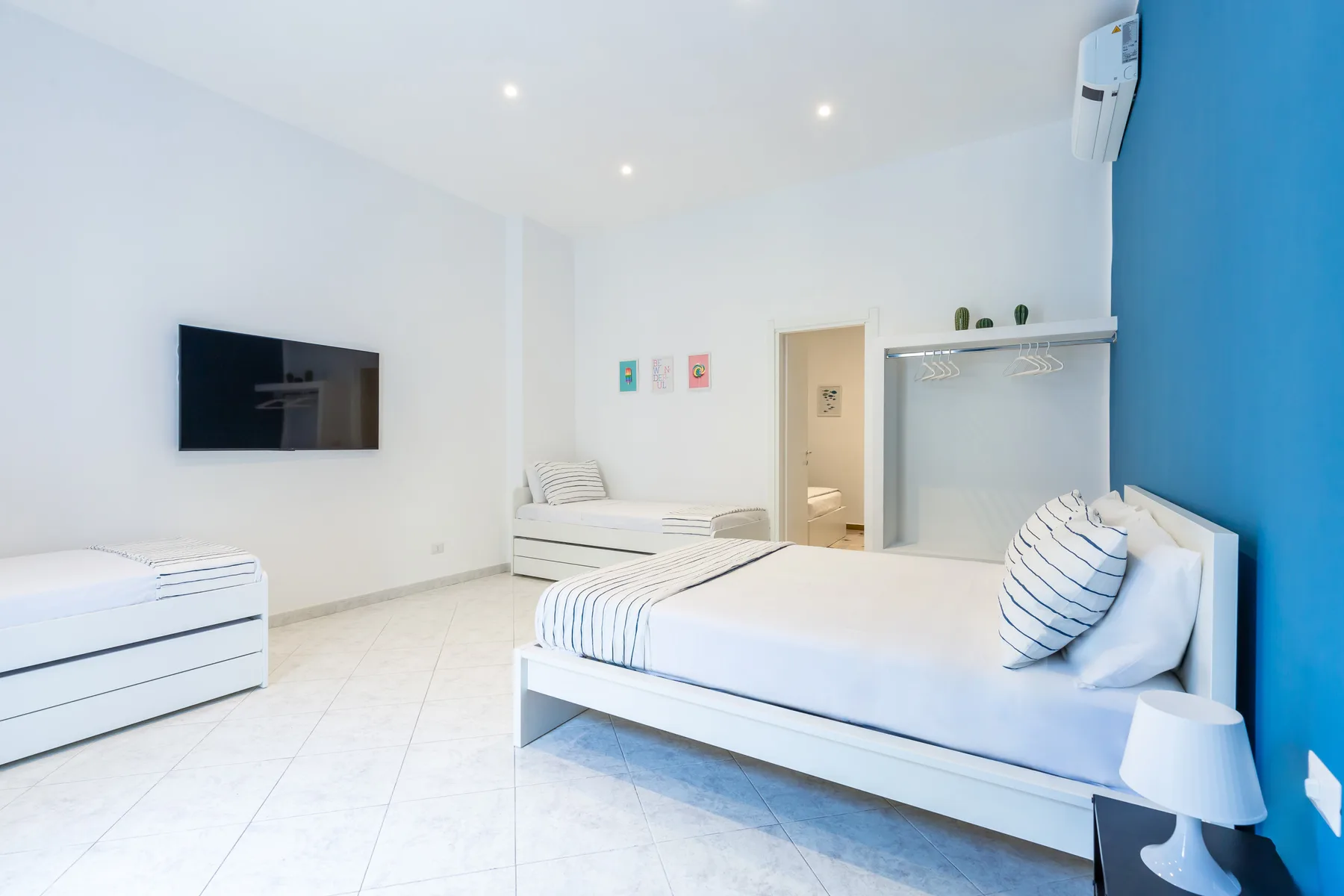 A bright bedroom with a bed, a wall-mounted television, and a clothes rack.