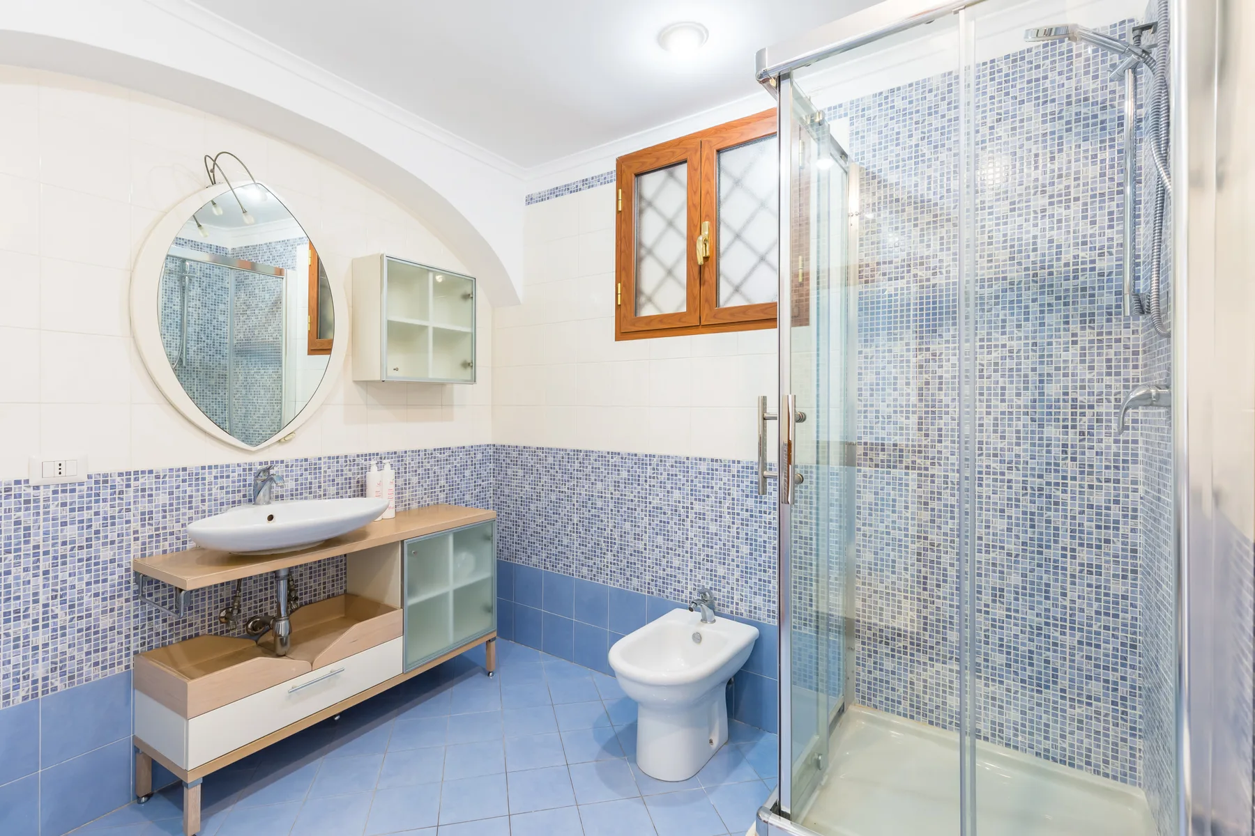 A tiled bathroom with a glass shower, sink, and toilet.