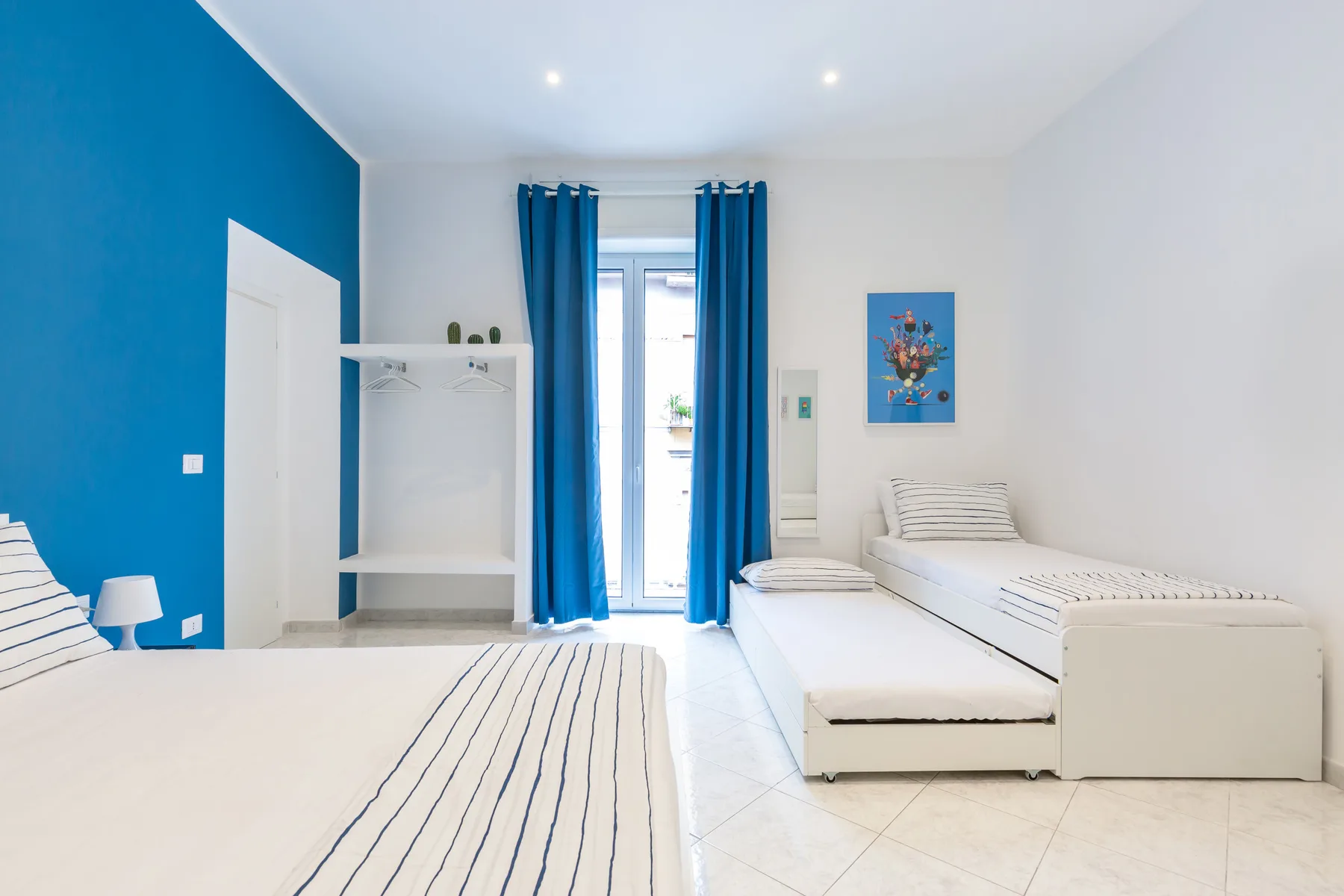 A bright bedroom with blue curtains and beds arranged along the walls.