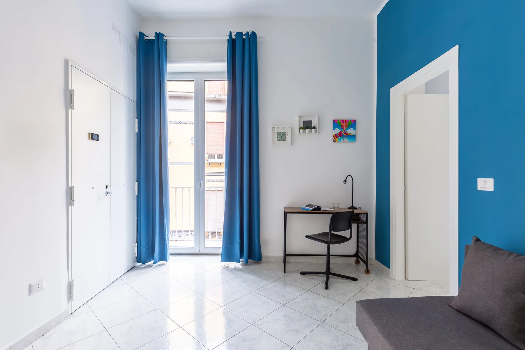 A bright room with a desk beside a tall window and blue curtains.