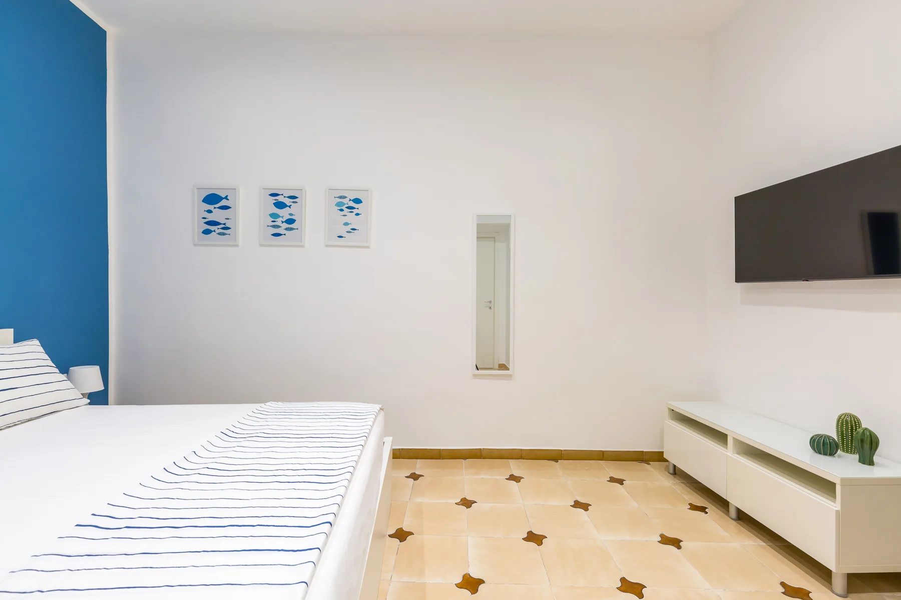 A bedroom with a bed, a blue accent wall, and a low television cabinet.