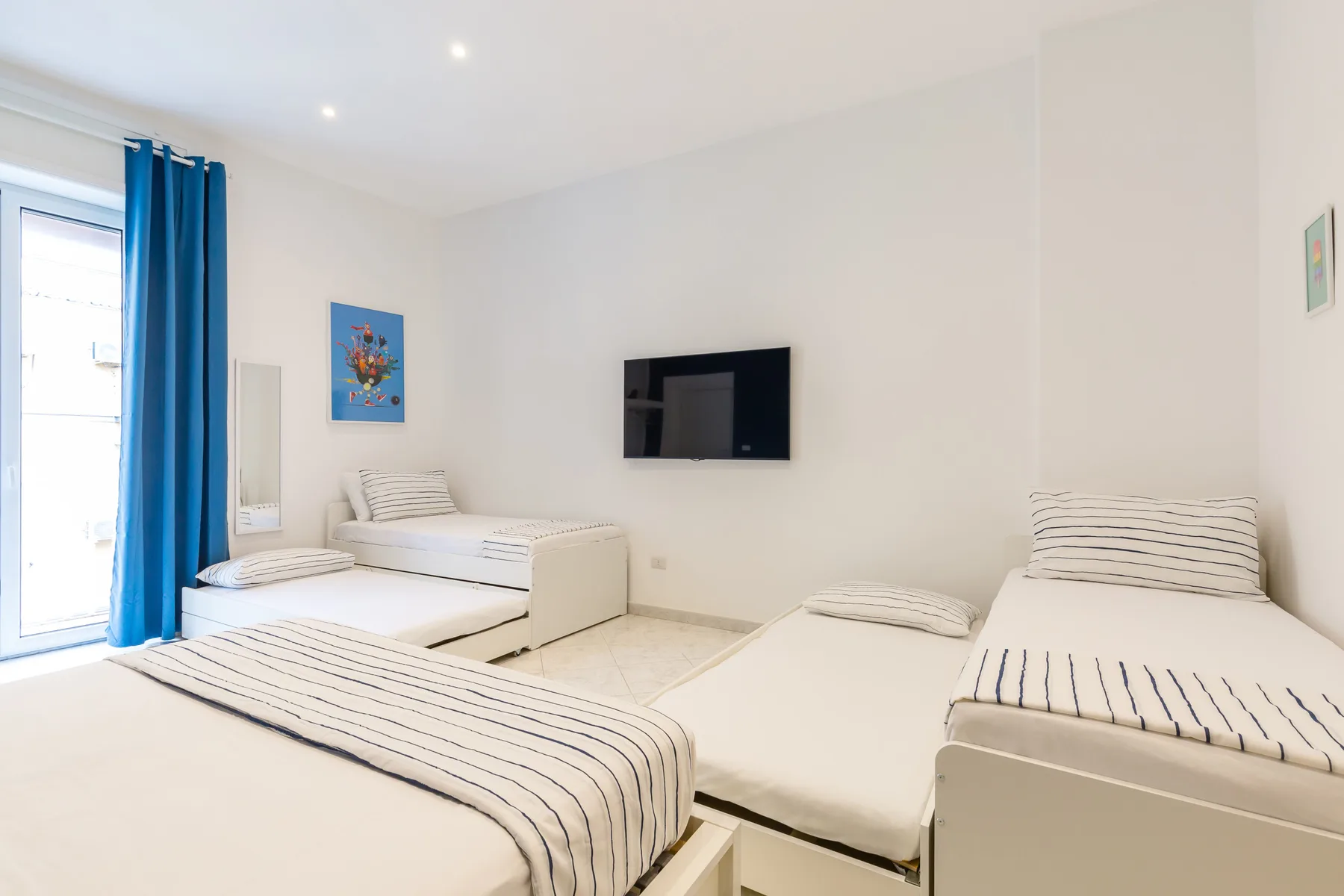 A bright bedroom with striped bedding and a wall-mounted television.