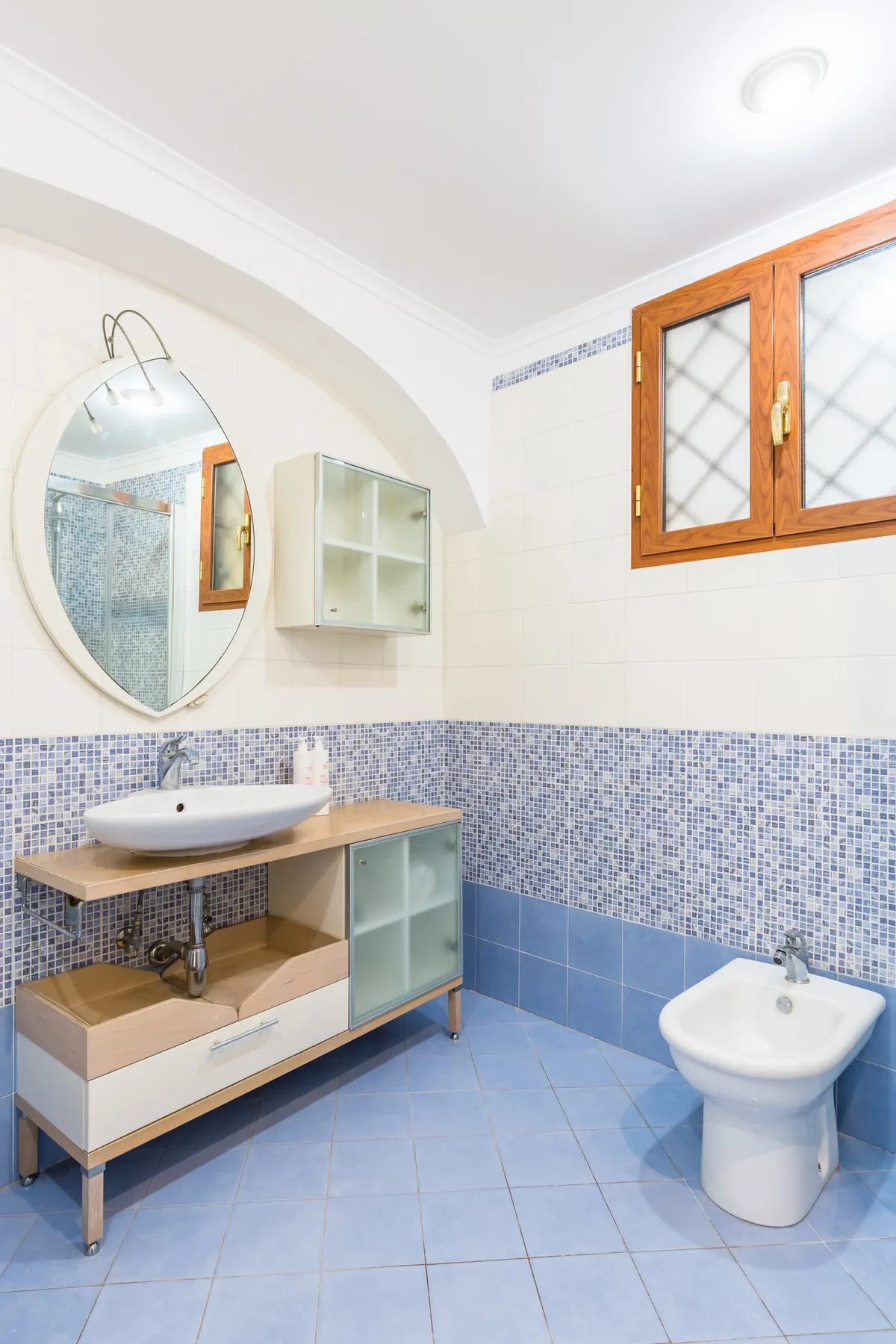 A bathroom with a vanity, round mirror, and a toilet.