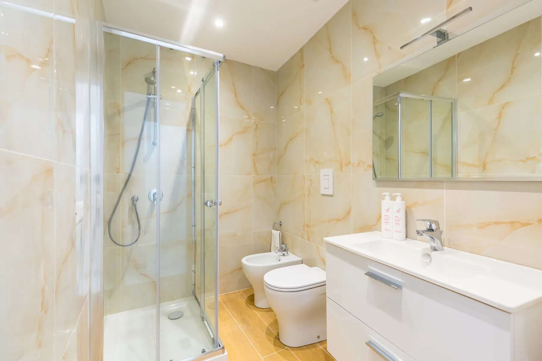 A tiled bathroom with a glass shower, toilet, and sink vanity.