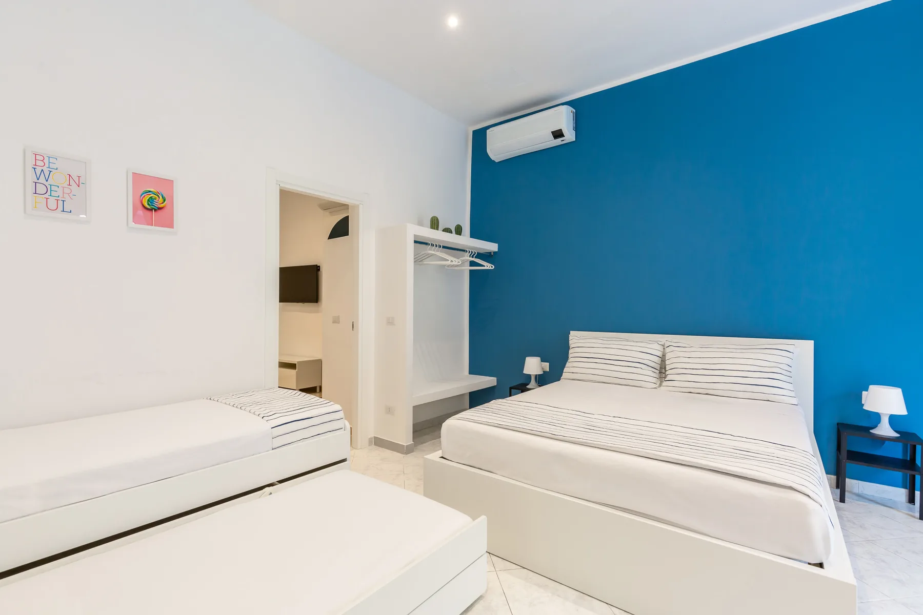 A bedroom with a large bed, a single bed, and a blue accent wall.