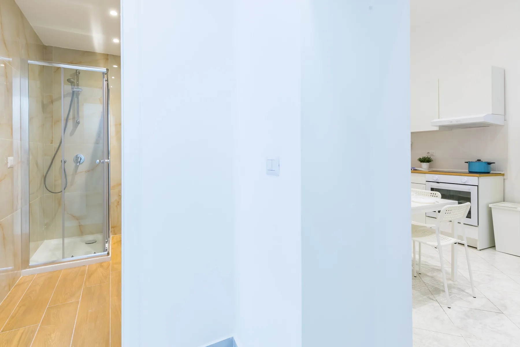 A bathroom with a glass shower and a kitchen visible through the doorway.