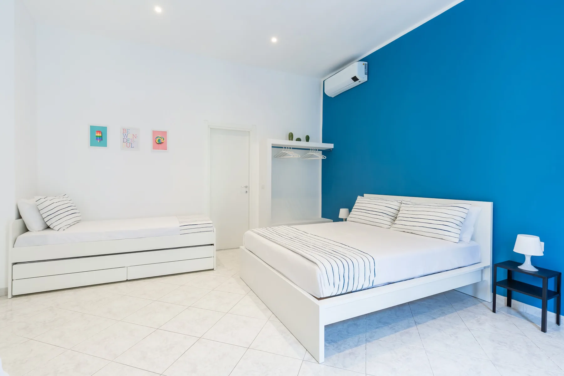 A bright bedroom with a double bed and a single bed against a blue wall.