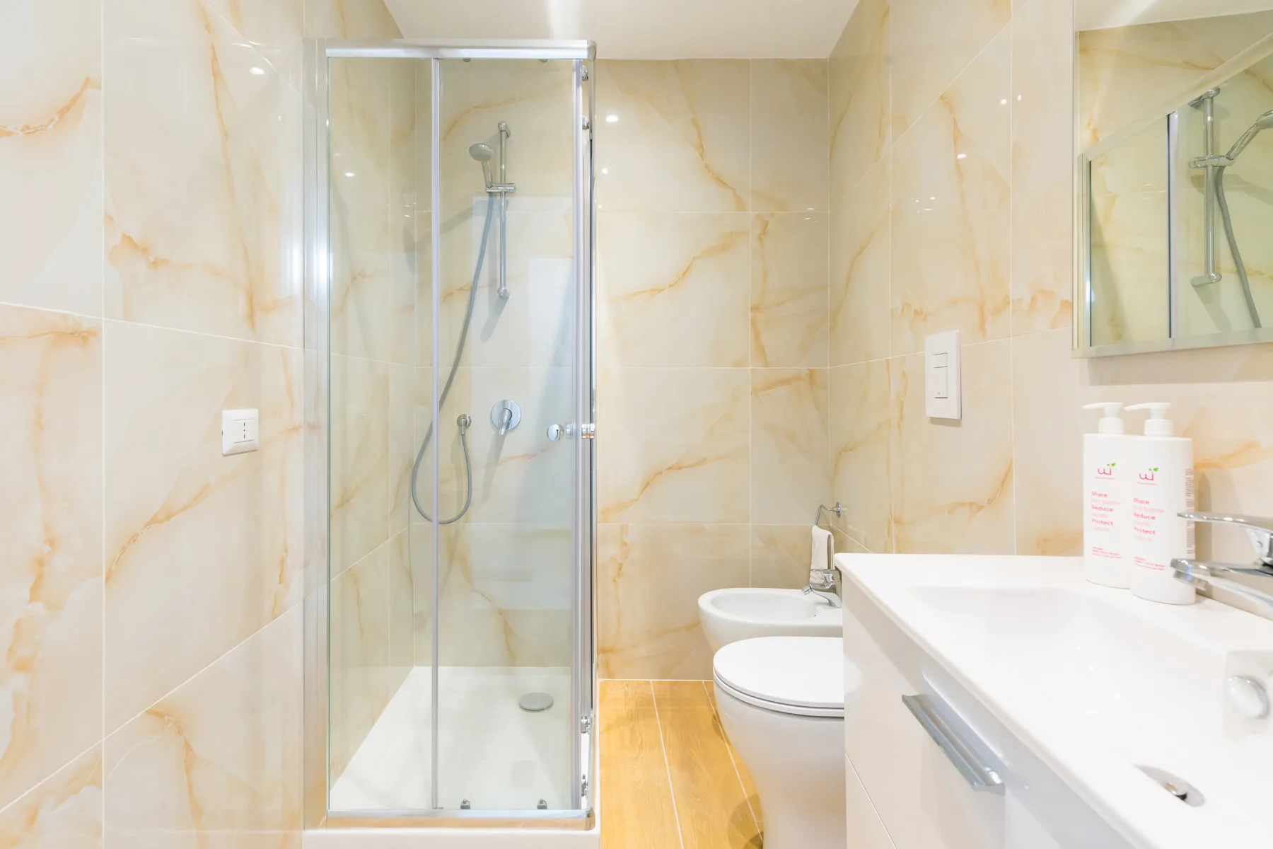 A tiled bathroom with a glass shower, toilet, and sink.