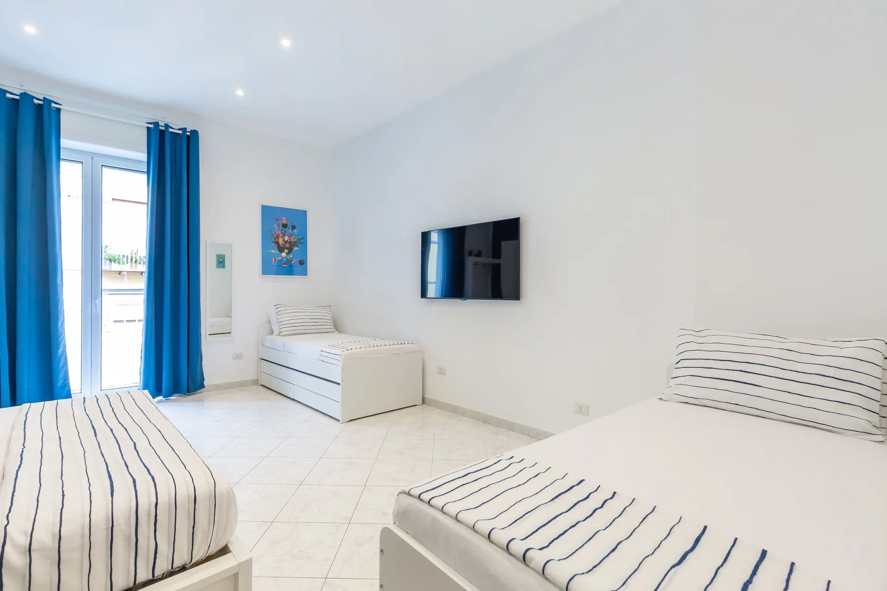 A bright bedroom with striped bedding and a wall-mounted television.