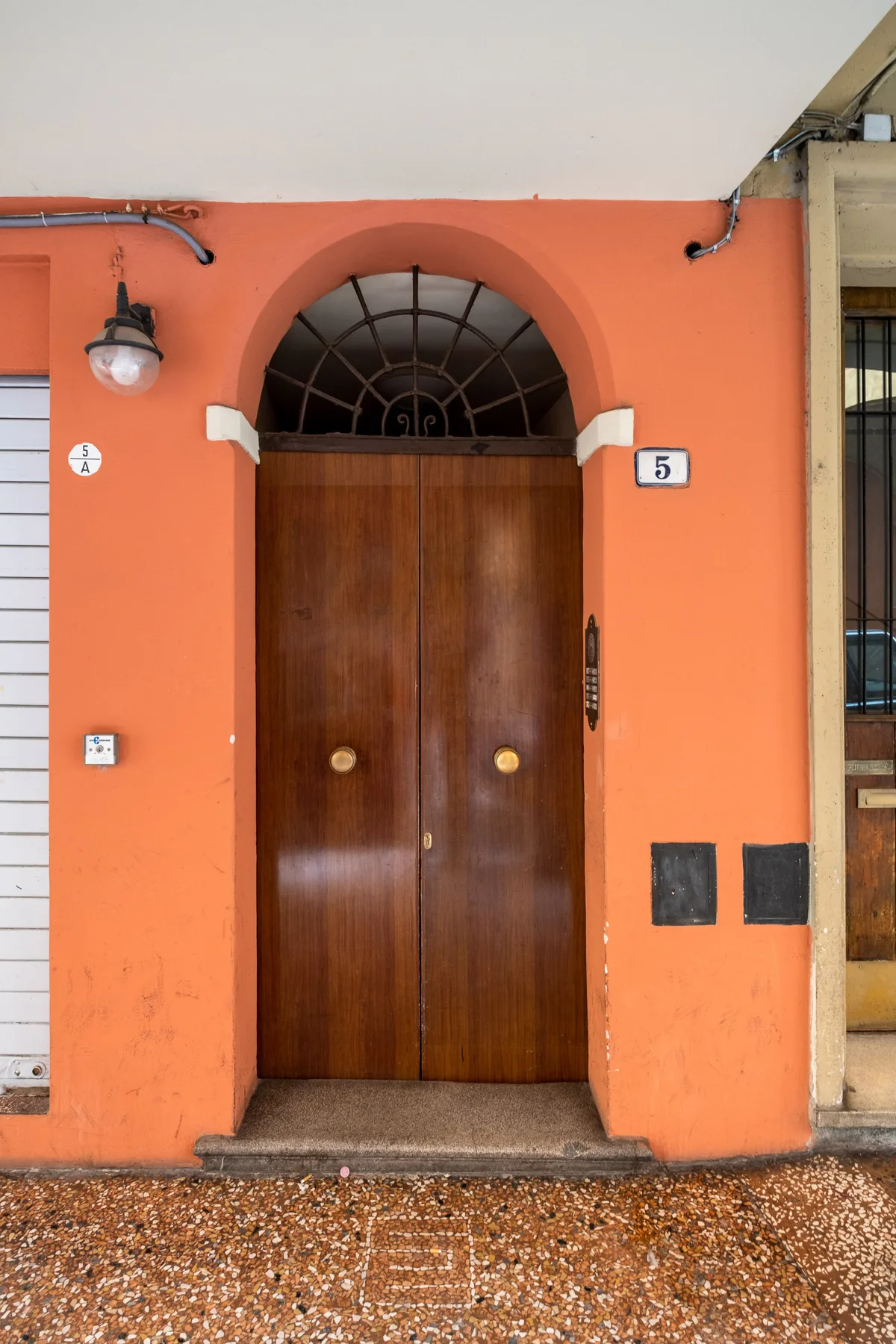 An arched wooden entrance door set in an orange exterior wall.