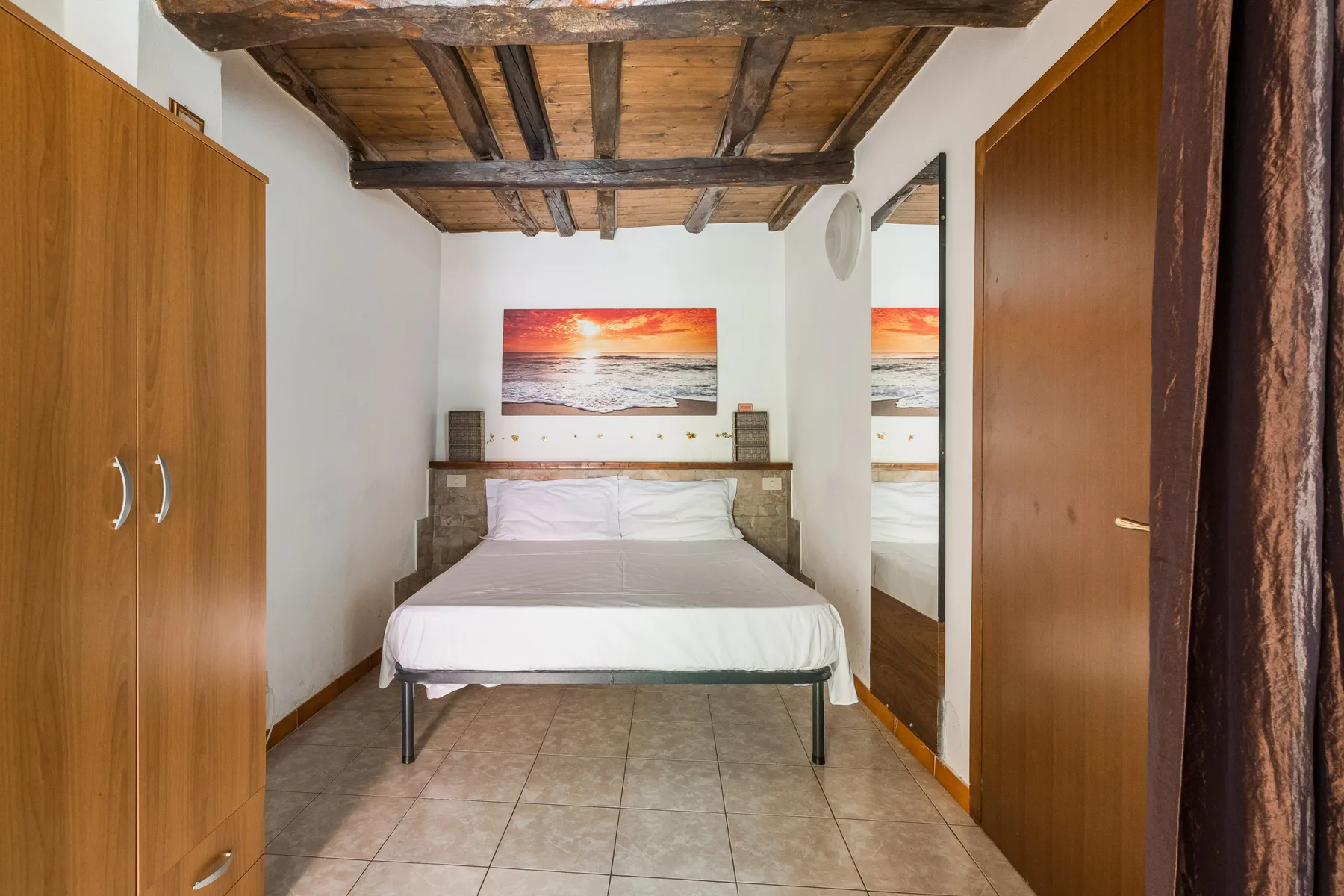 A bedroom with a bed beneath exposed wooden ceiling beams.