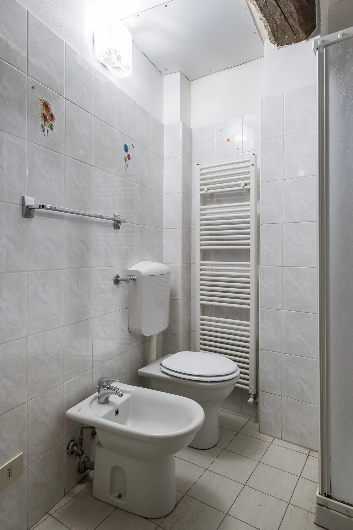 A tiled bathroom with a toilet, bidet, and wall-mounted towel warmer.