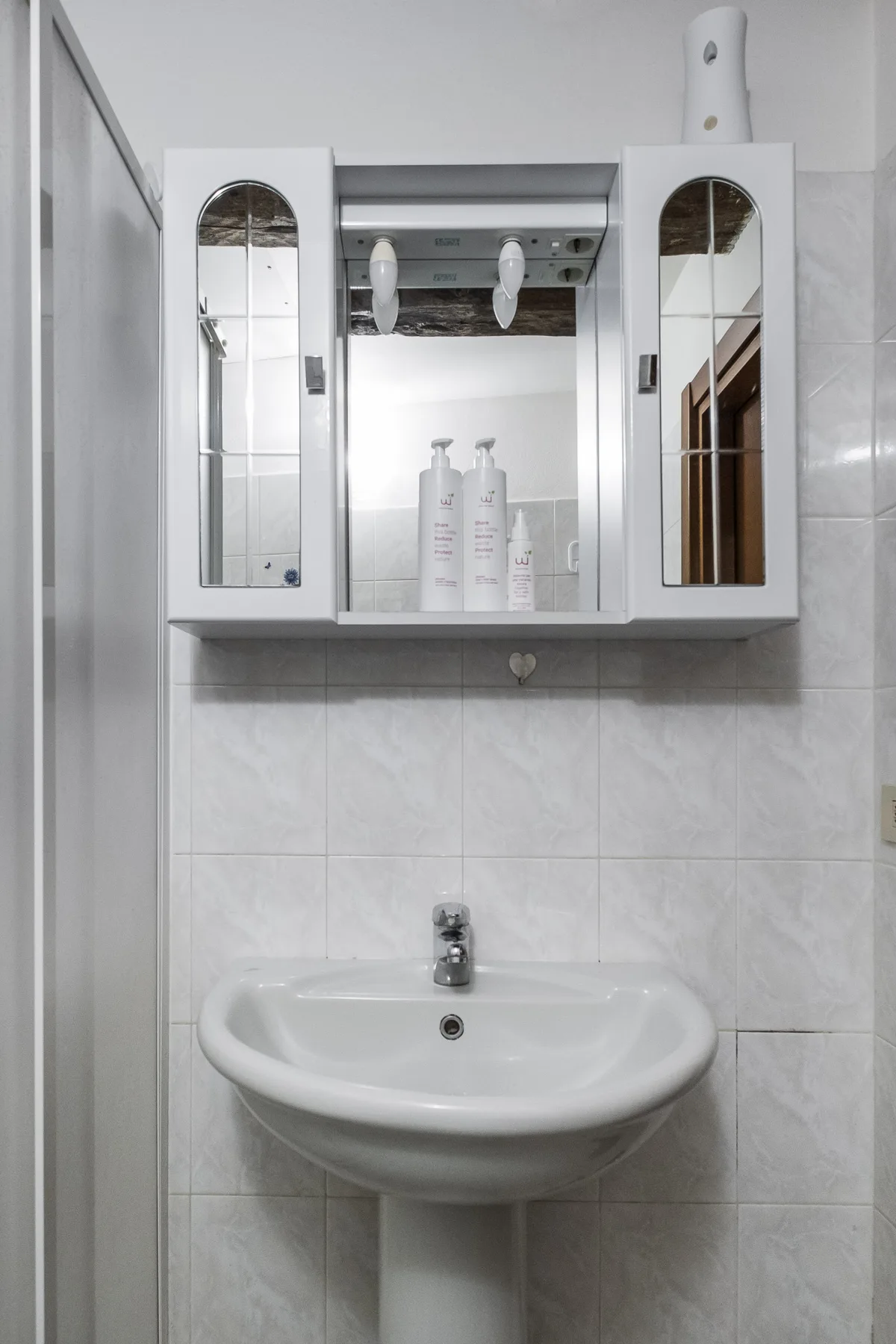 A bathroom sink beneath a mirrored wall cabinet against tiled walls.