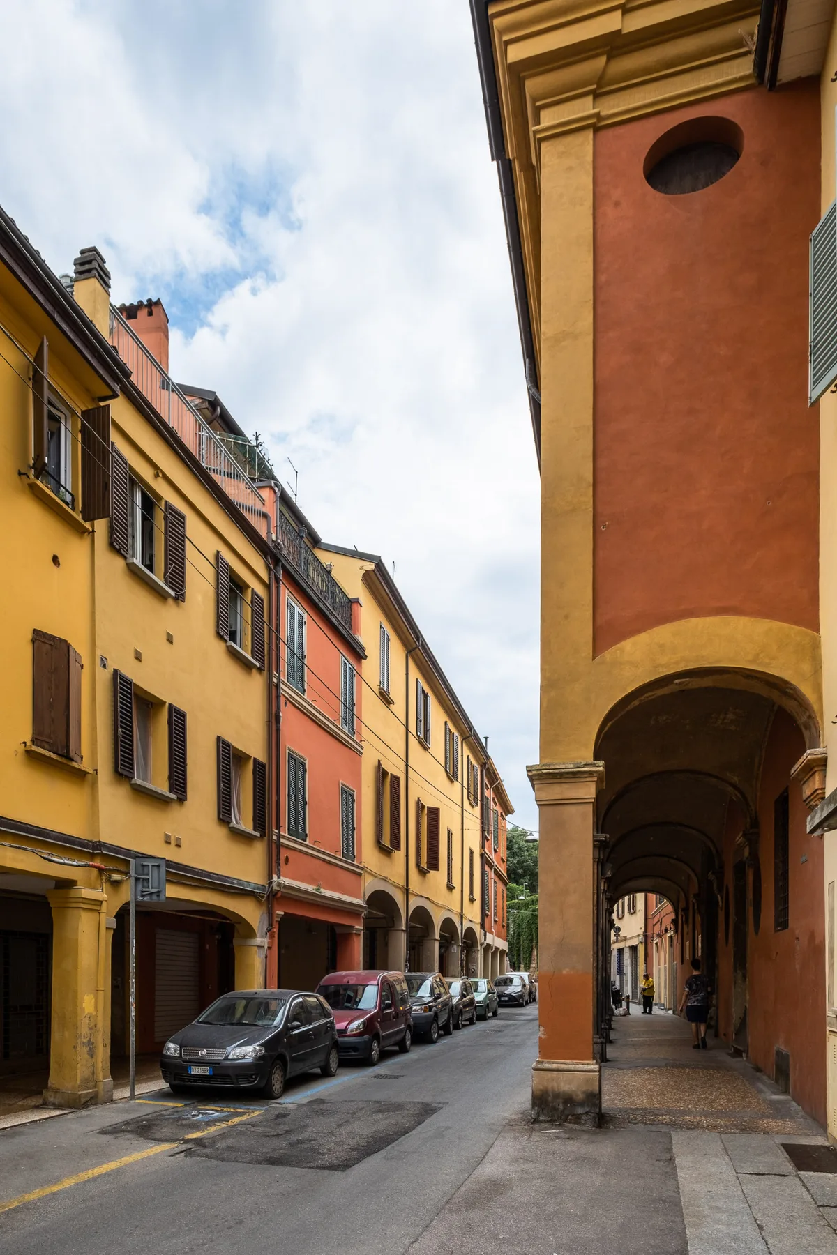A narrow street lined with colorful buildings and parked cars.