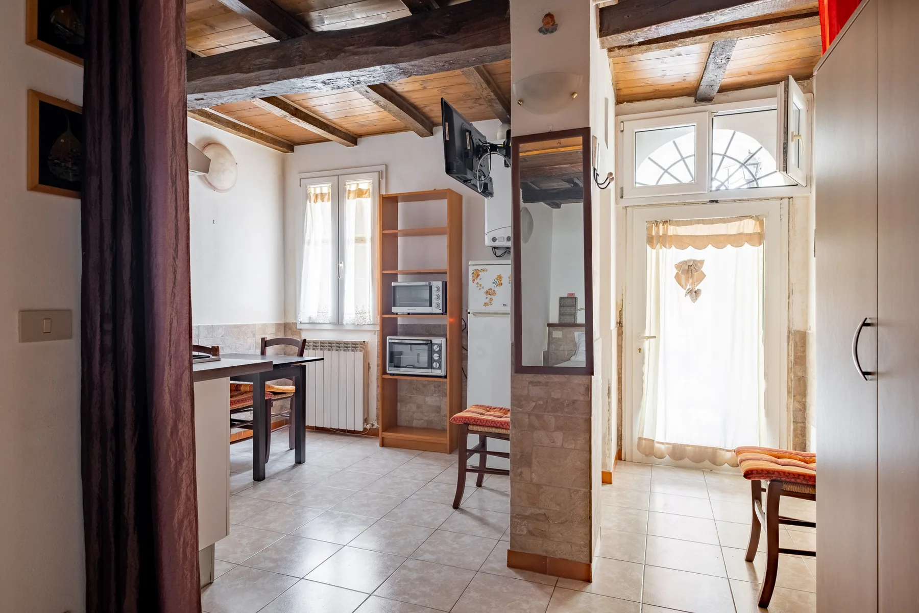 A bright kitchen and dining area with a table, appliances, and exposed ceiling beams.