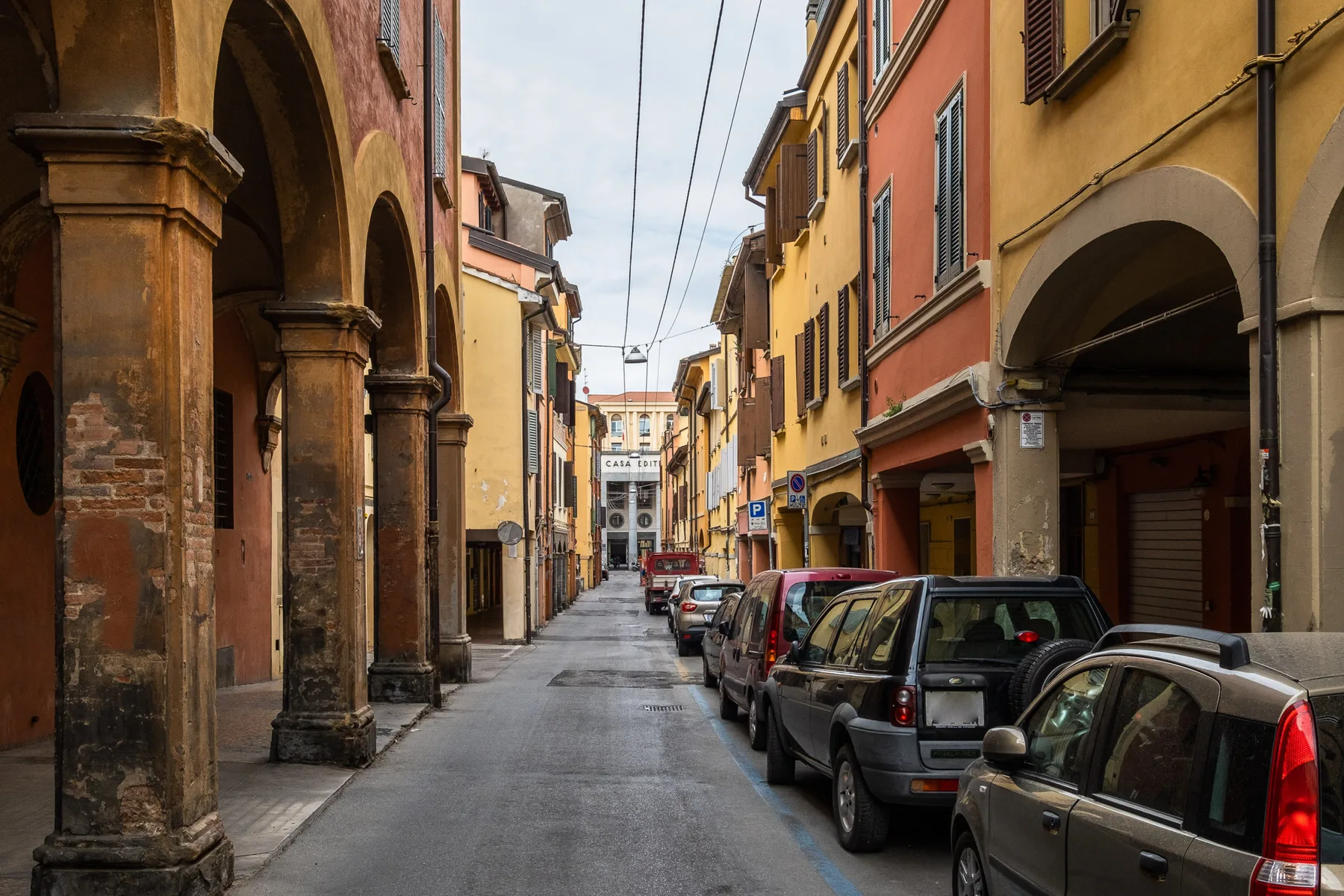 A narrow city street lined with colorful buildings and parked cars.