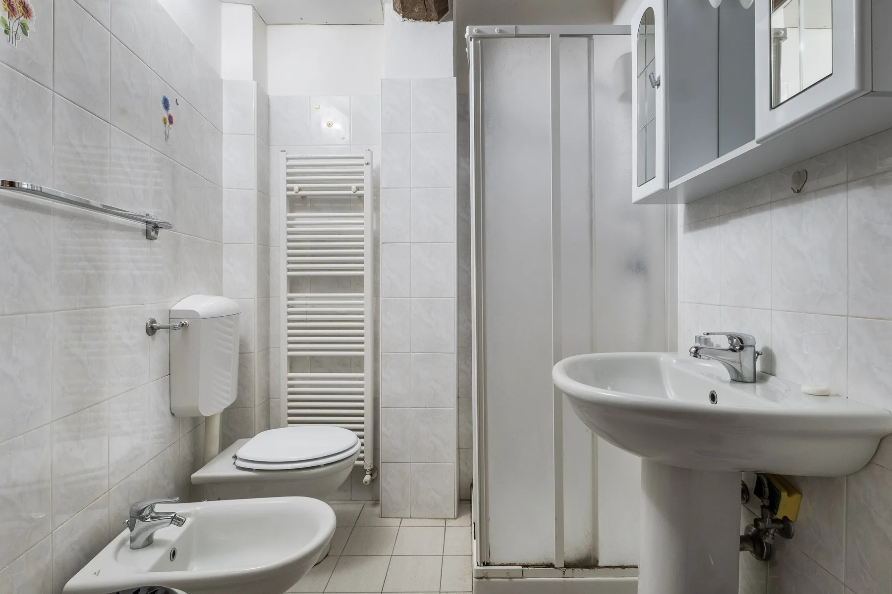 A tiled bathroom with a shower, sink, toilet, and bidet.