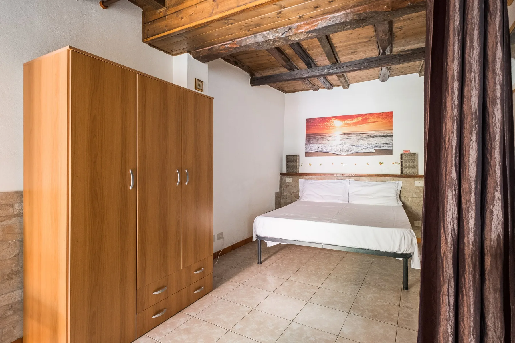 A bedroom with a bed, wooden wardrobe, and exposed wooden ceiling beams.