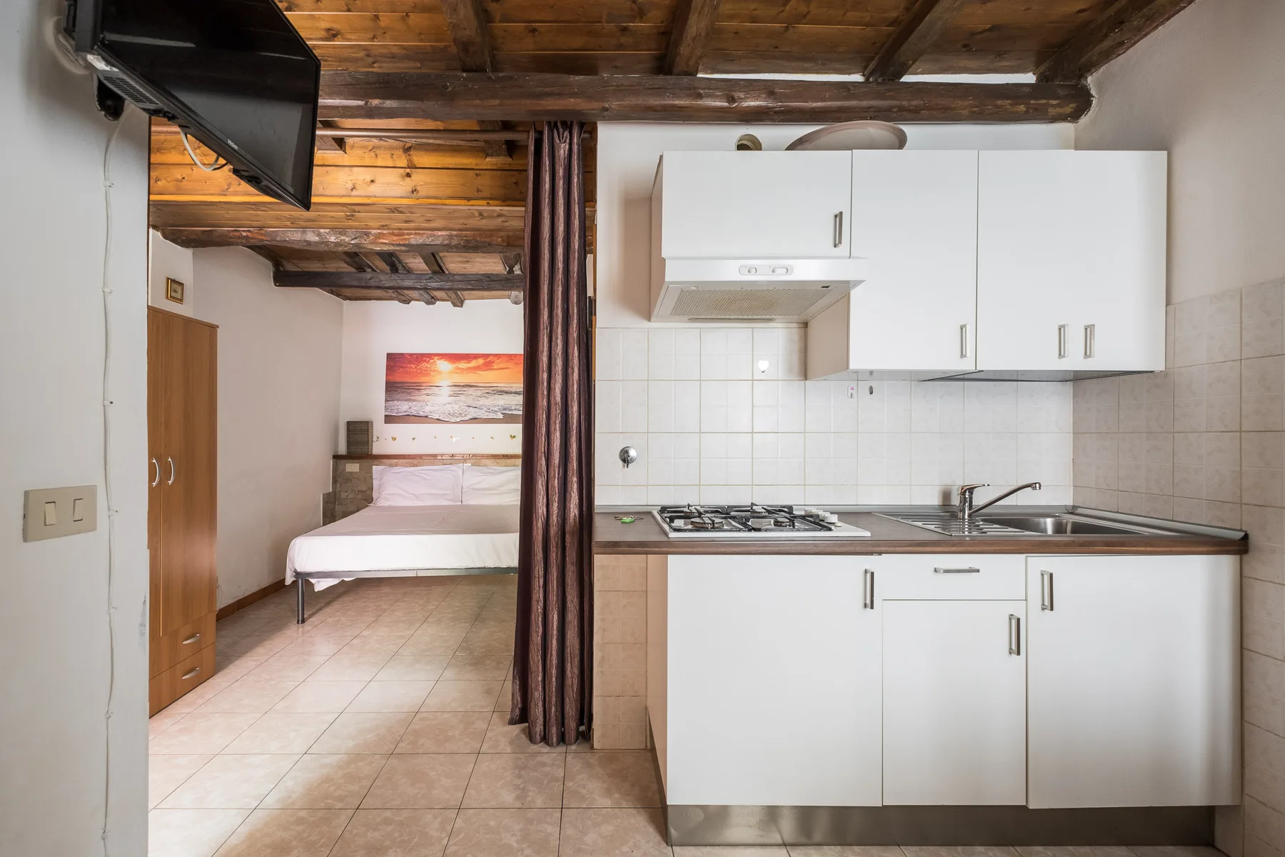 A compact kitchen with white cabinets and a sleeping area beyond a curtain.