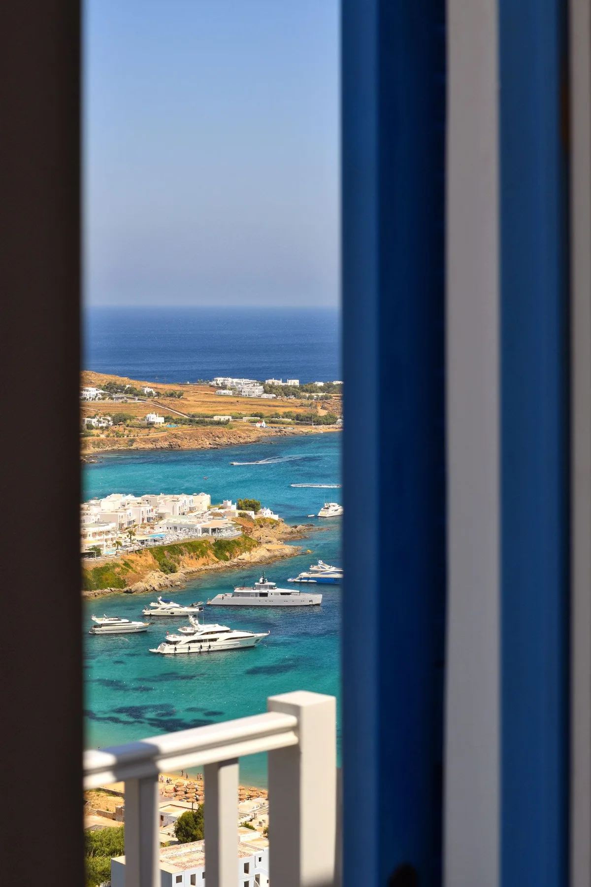 A coastal view shows turquoise water, boats, and buildings beyond a balcony railing.