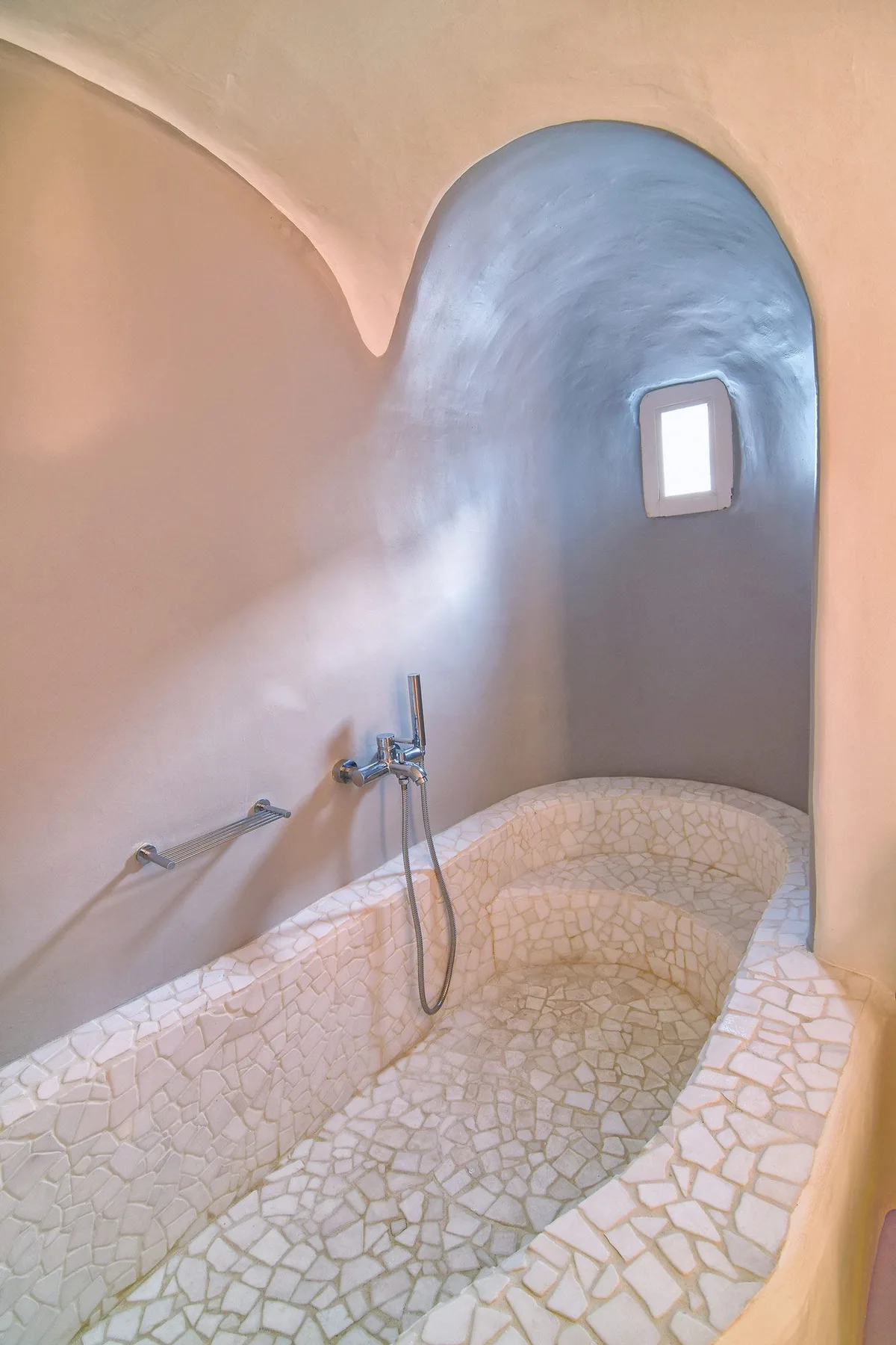 A curved tiled bathtub sits beneath an arched blue wall niche.