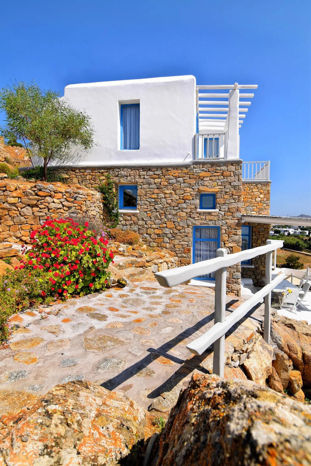 A stone house with white upper walls stands beside a rocky garden path.