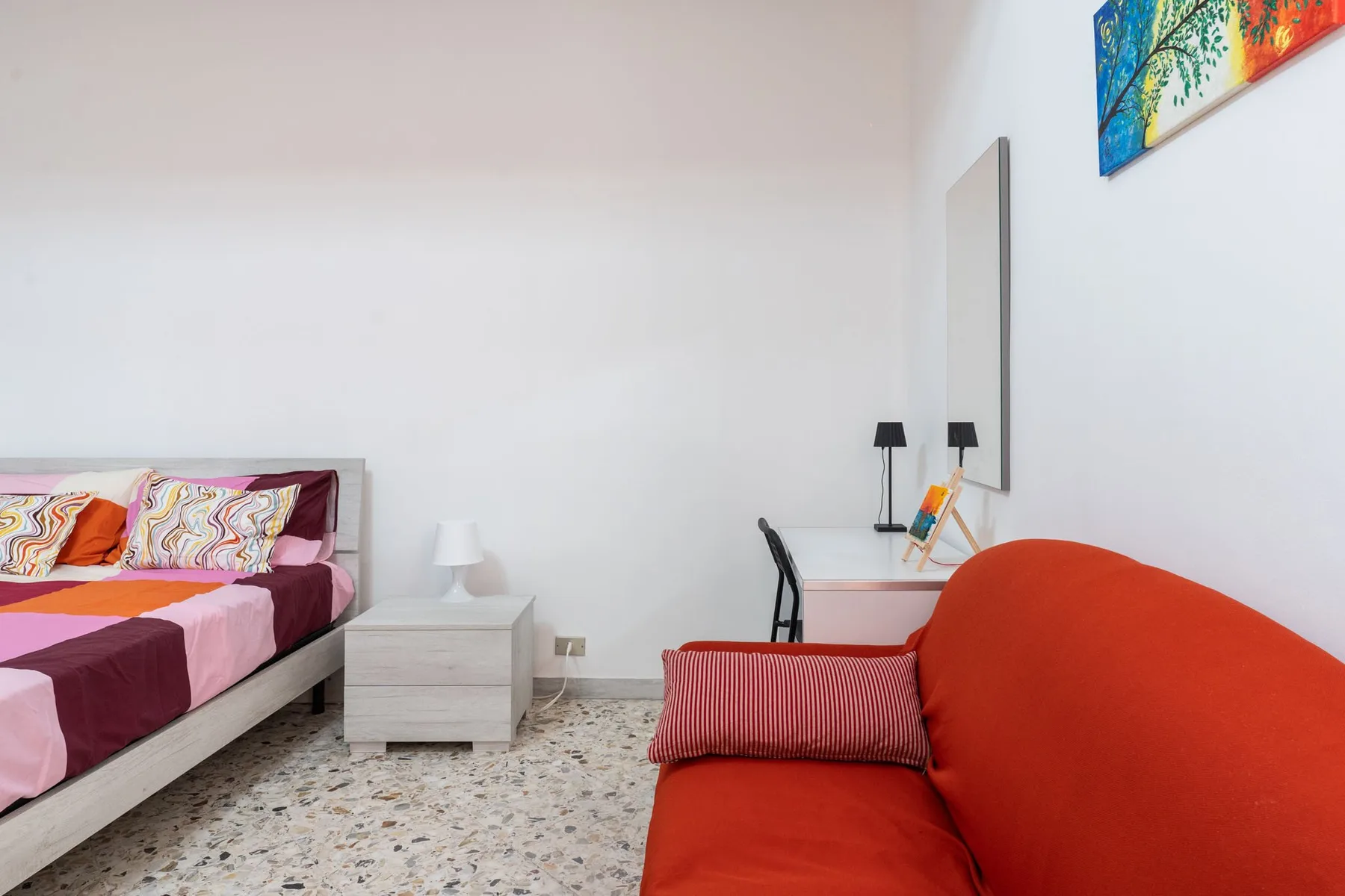 A colorful bedroom with a bed, bedside table, and red seating.