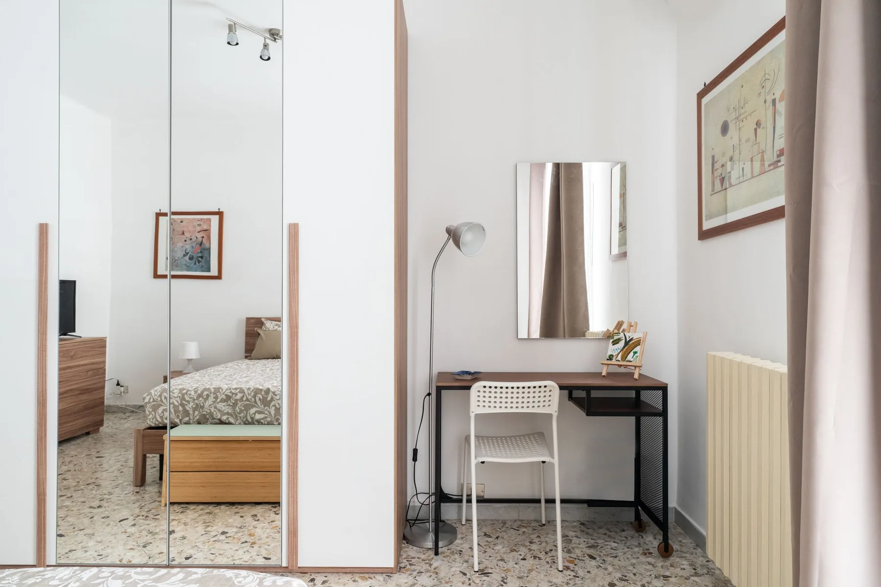 A bright bedroom with a desk, chair, and mirrored wardrobe.
