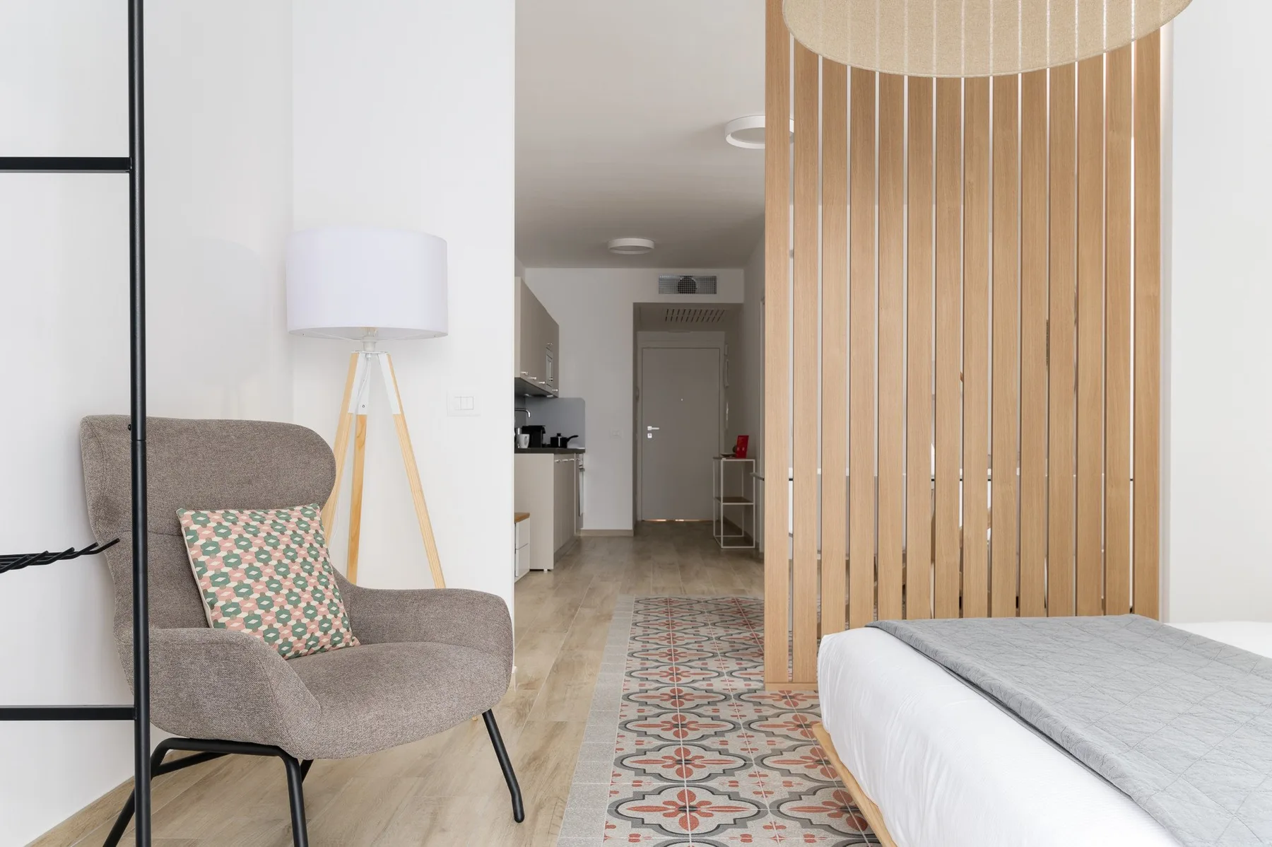 A bedroom with a bed, a seating area, and a wooden slat divider.