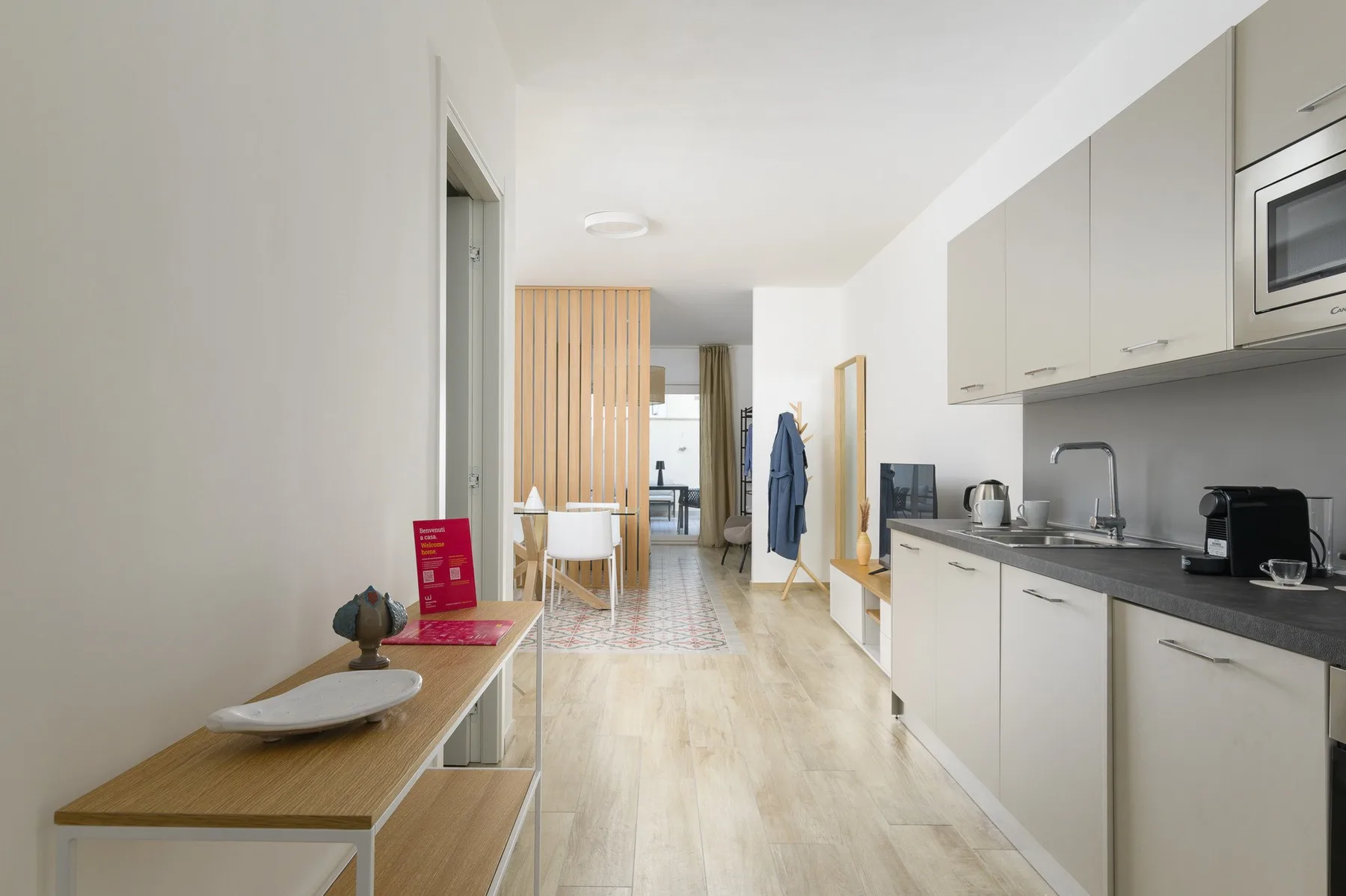 A bright kitchenette and dining area with light wood flooring and a narrow table.