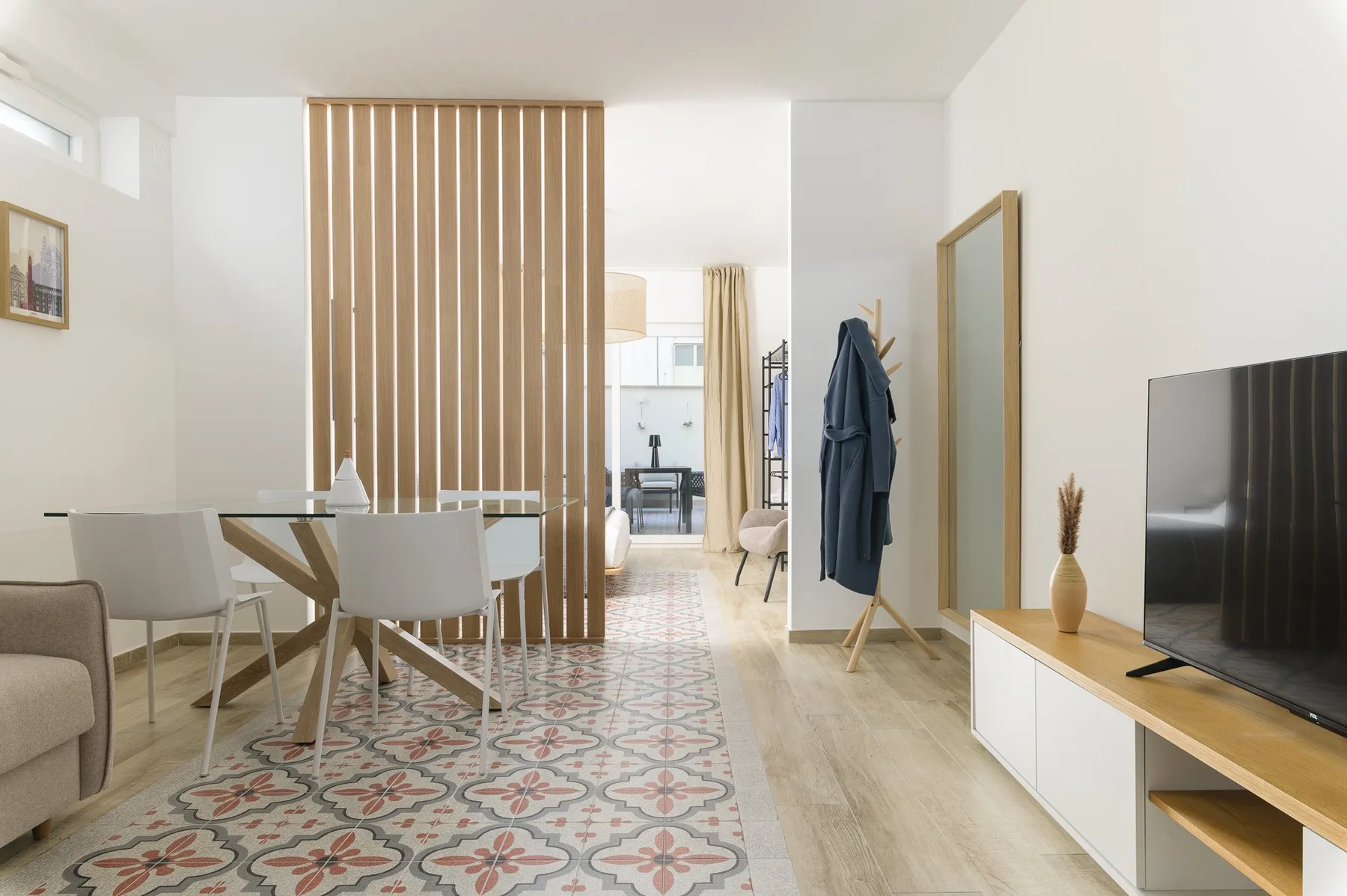 A bright living and dining area with patterned floor tiles and a television.