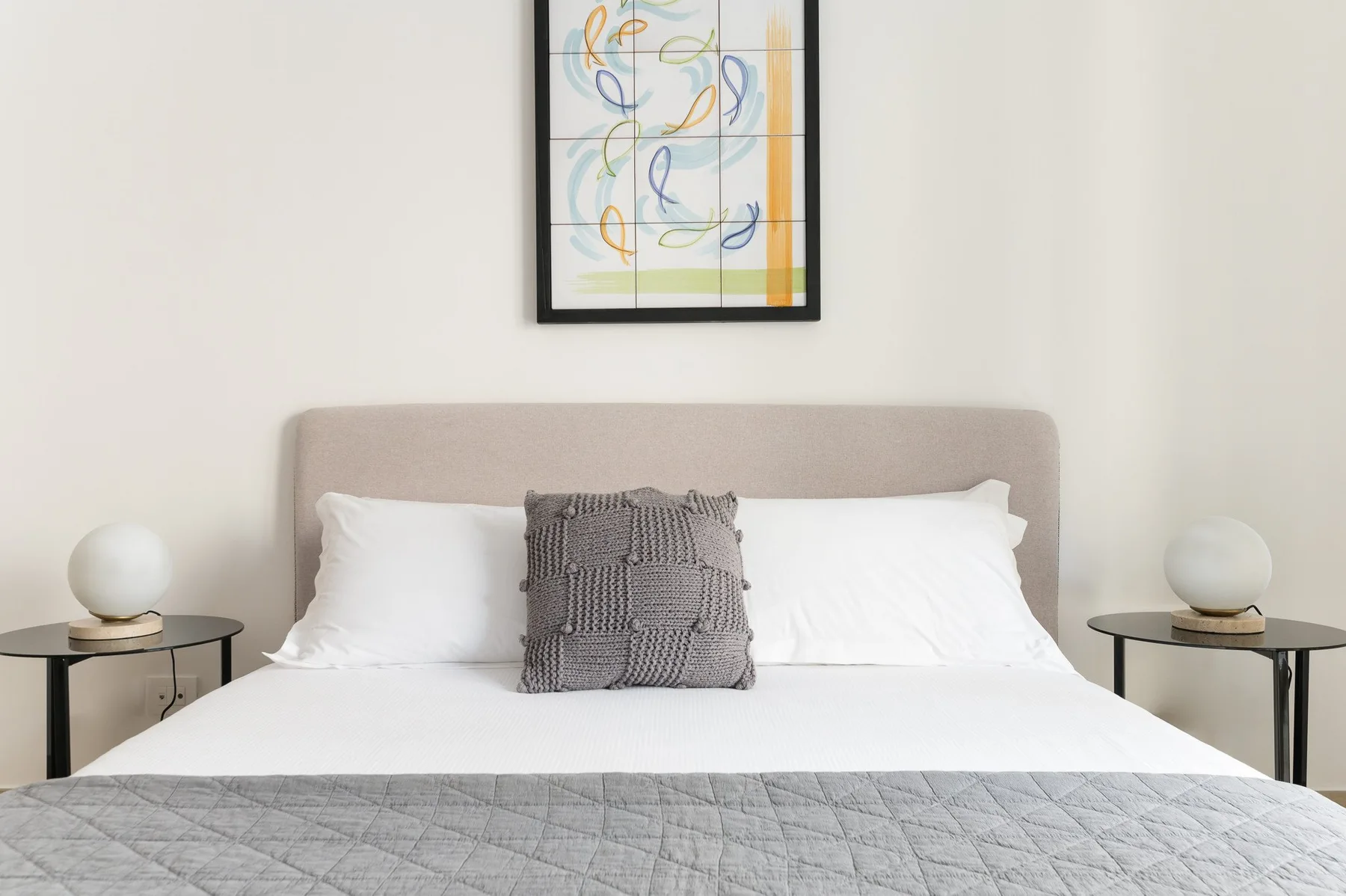 A bedroom with a neatly made bed and framed abstract artwork above the headboard.