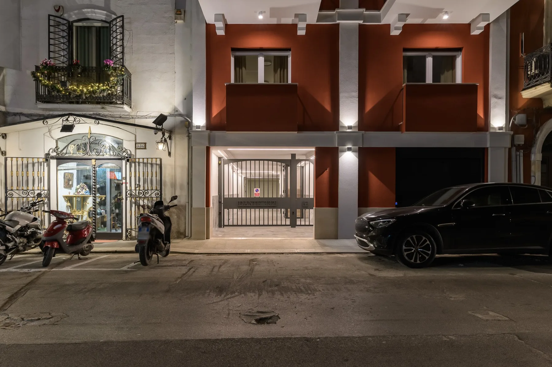A nighttime street view shows a gated building entrance and parked vehicles.
