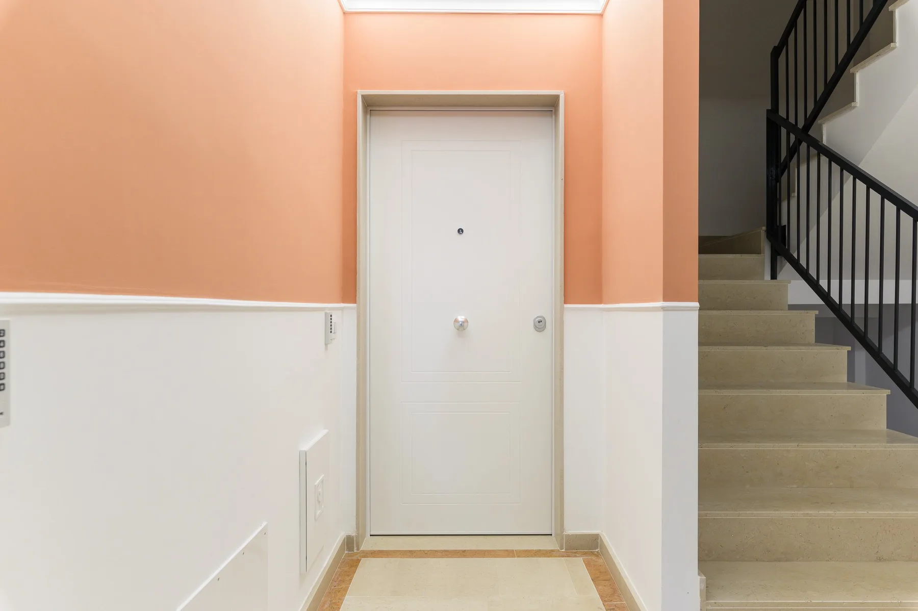 An interior hallway with a white door and a staircase beside it.