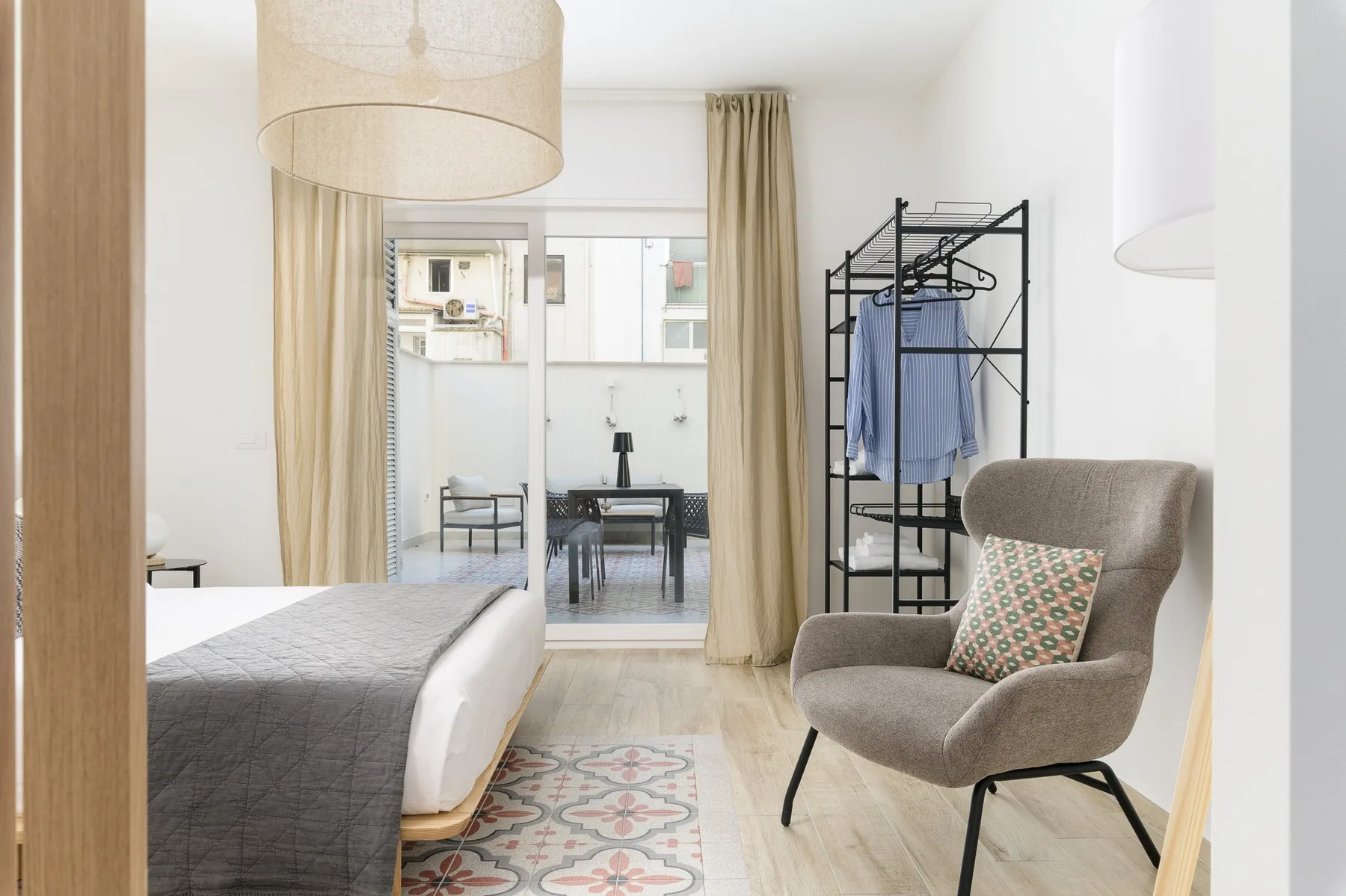 A bright bedroom with a bed, seating, and a clothing rack beside the window.
